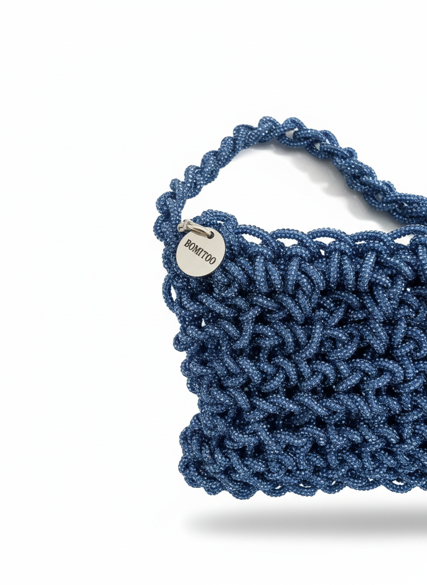 Blue handmade bag crafted with sparkling luminous thread, soft three-dimensional shape, braided handle and metal ring details.