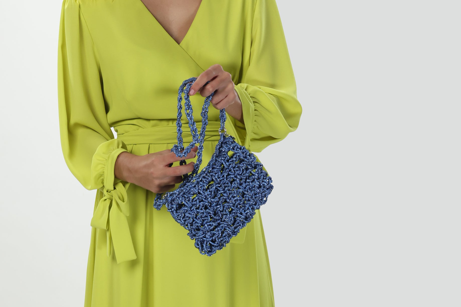 Blue handmade bag crafted with sparkling luminous thread, soft three-dimensional shape, braided handle and metal ring details held by a female model.