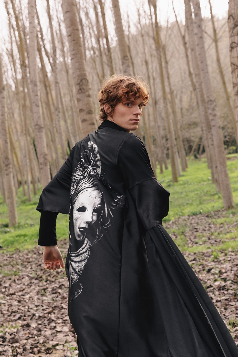 Black kimono worn by a model, featuring wide sleeves and a large black-and-white Venetian mask graphic on the back.