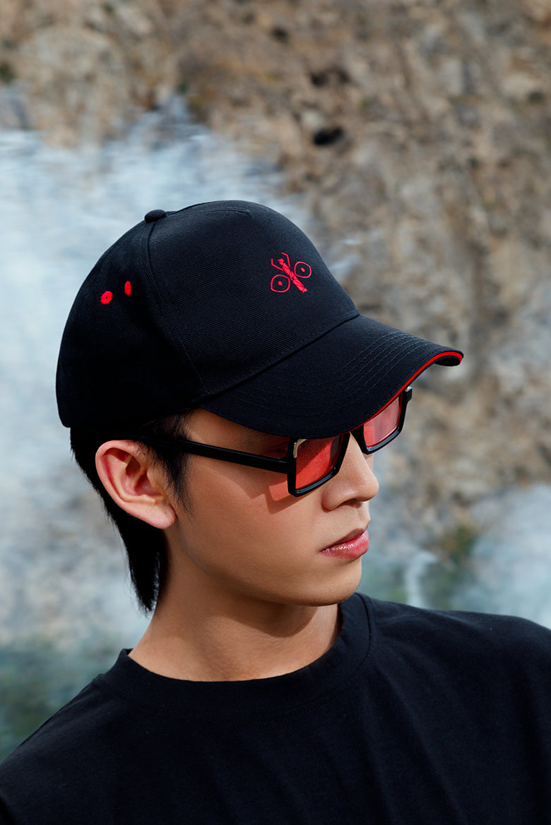 Black peaked cap with red embroidered logo worn by a model, showcasing its versatile and fashionable design.
