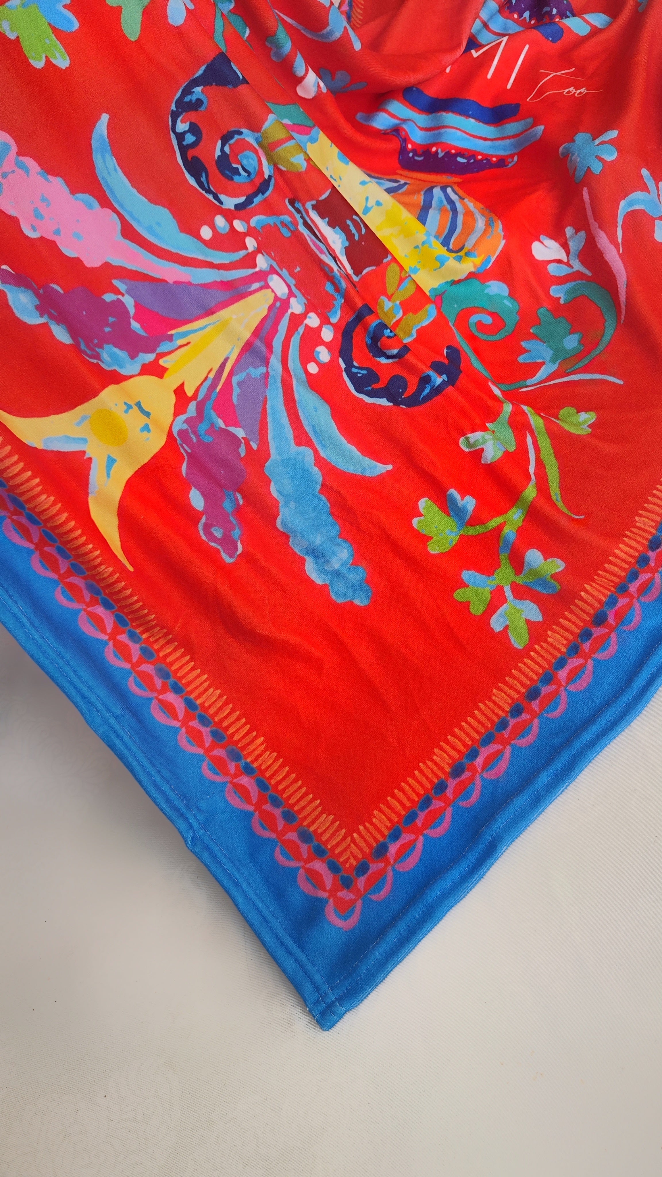 Close-up of the Sicilian-inspired print on the soft terry beach towel, highlighting red-orange colors and intricate patterns.