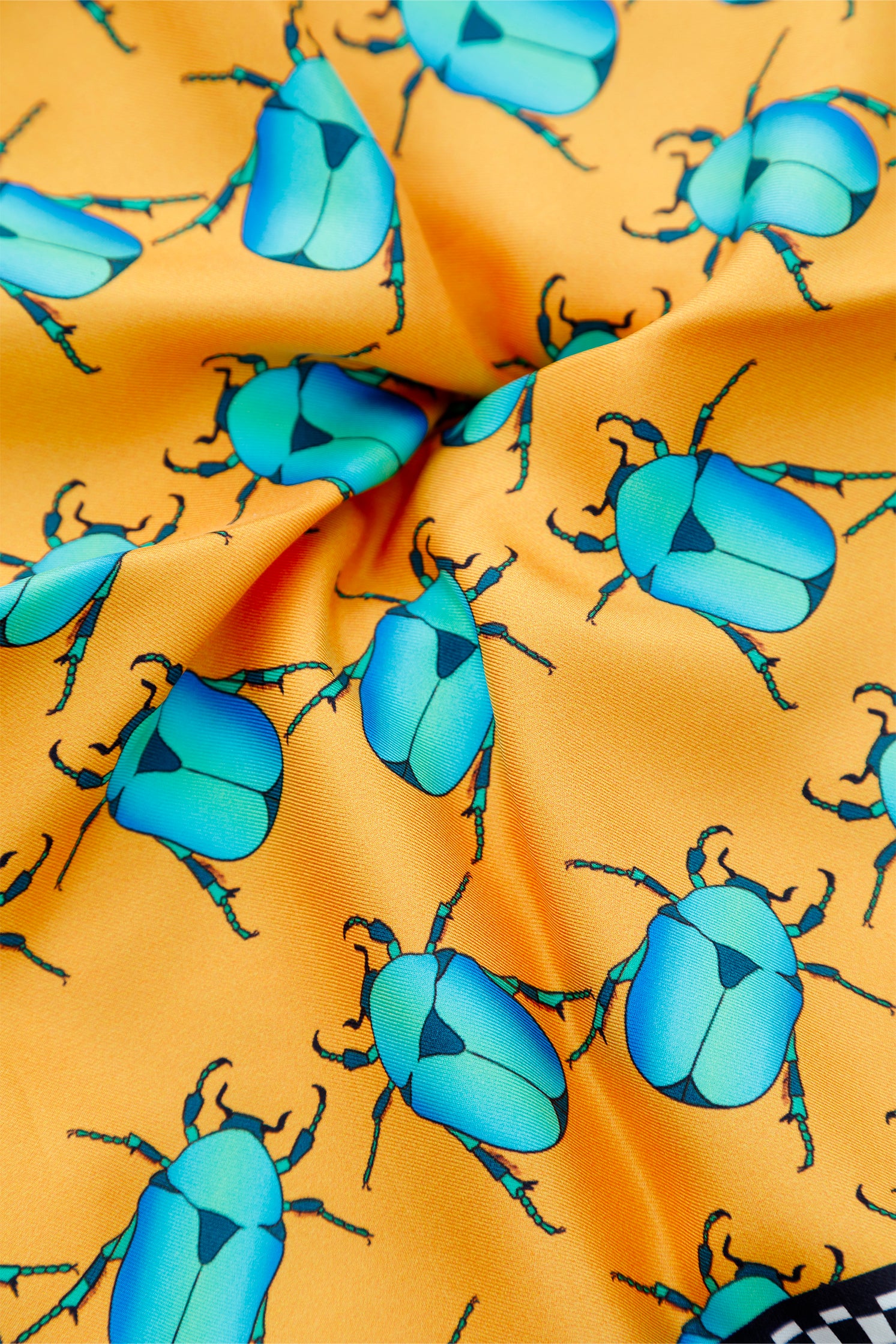Close-up of the orange silk scarf graphic featuring blue and black scarabs and black and white checkered border, showing intricate symbolic design.