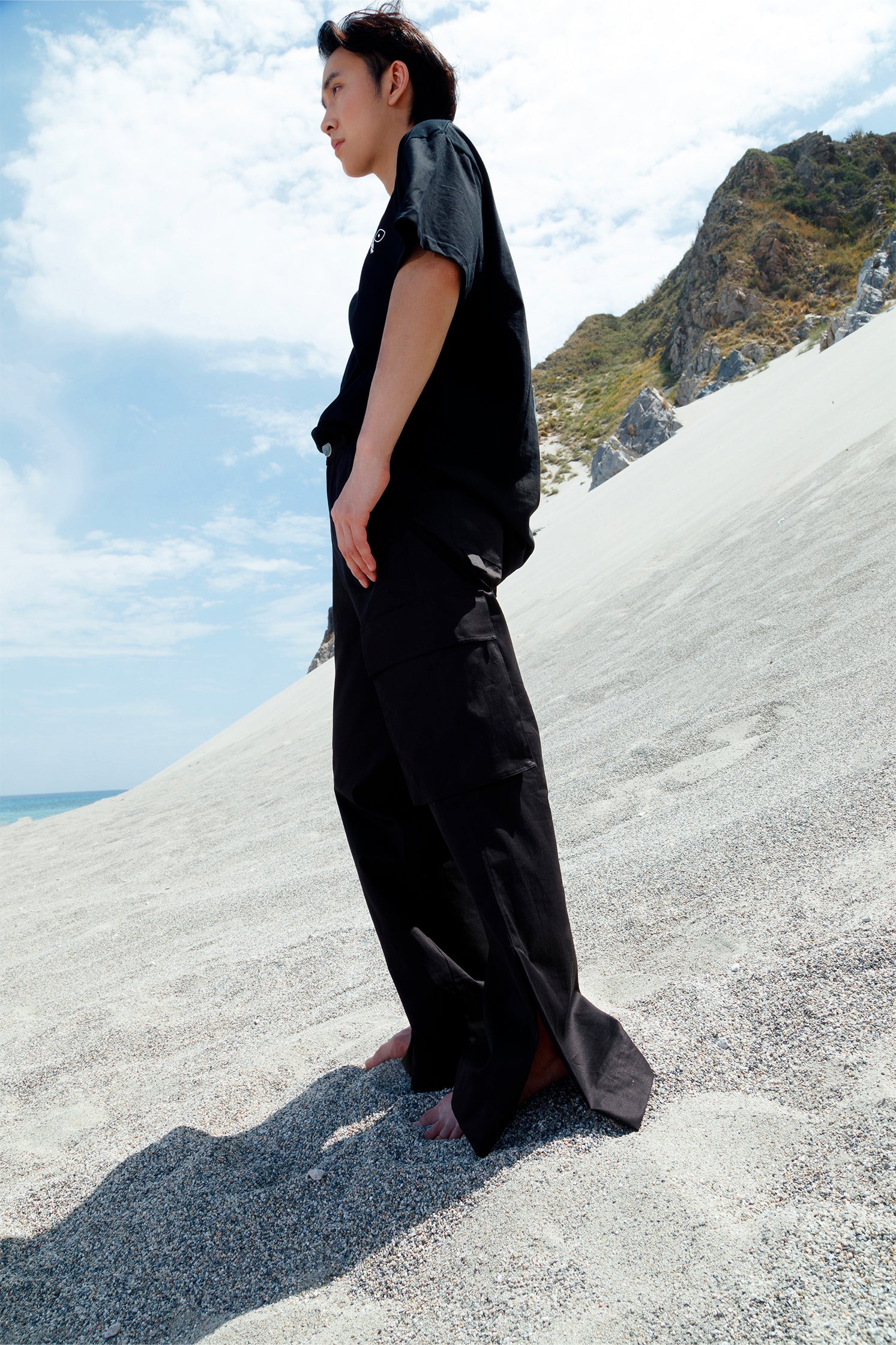 Side view of the unisex black cotton cargo pants worn by a model, featuring side patch pockets, relaxed fit, and small slit at the hem for added style and comfort.