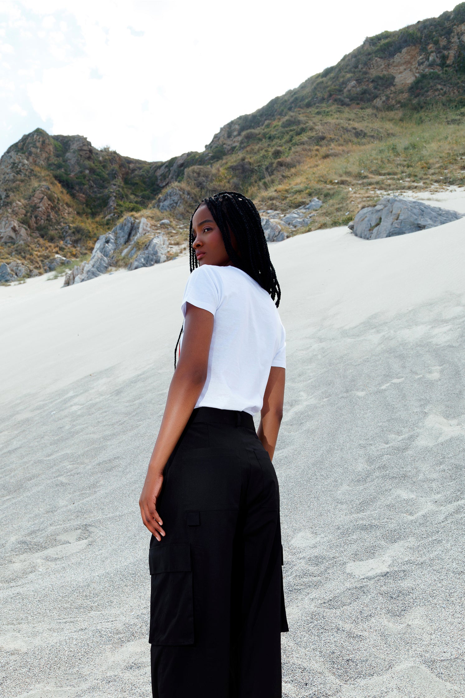 Back view of the unisex black cotton cargo pants worn by a model, featuring side patch pockets, relaxed fit, and small slit at the hem for added style and comfort.