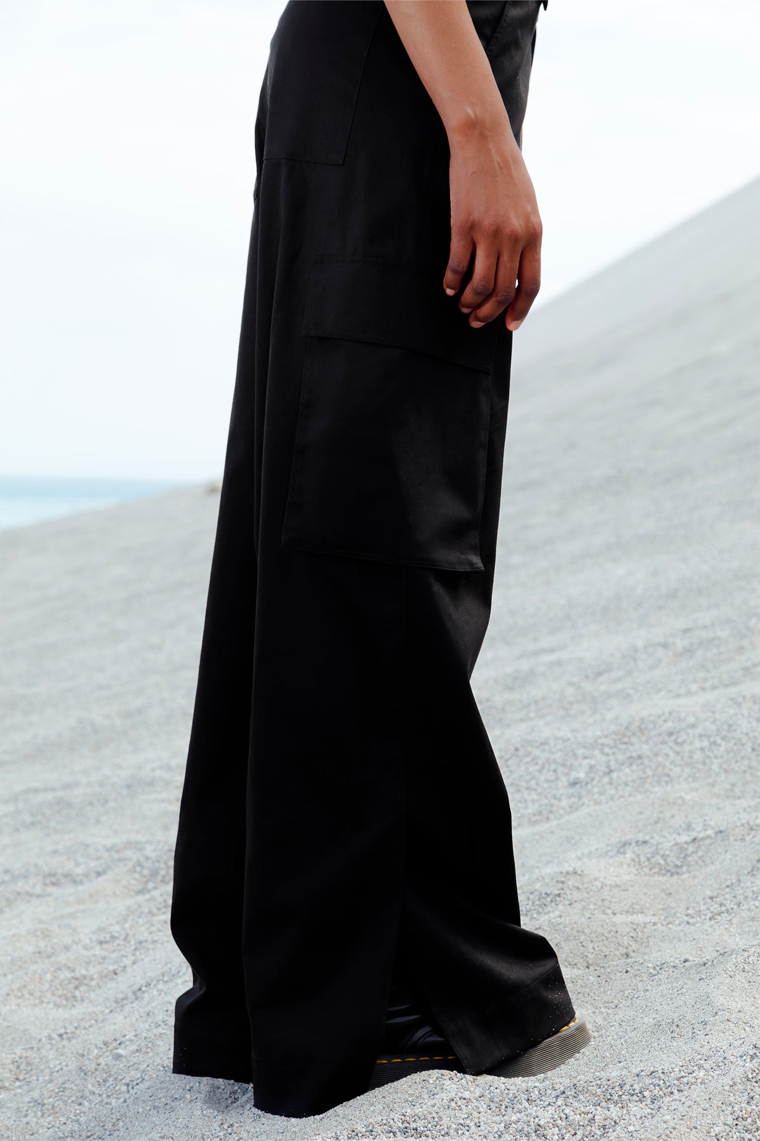 Close-up of the slit at the hem of the black cotton cargo pants, showing subtle design detail and relaxed fit.