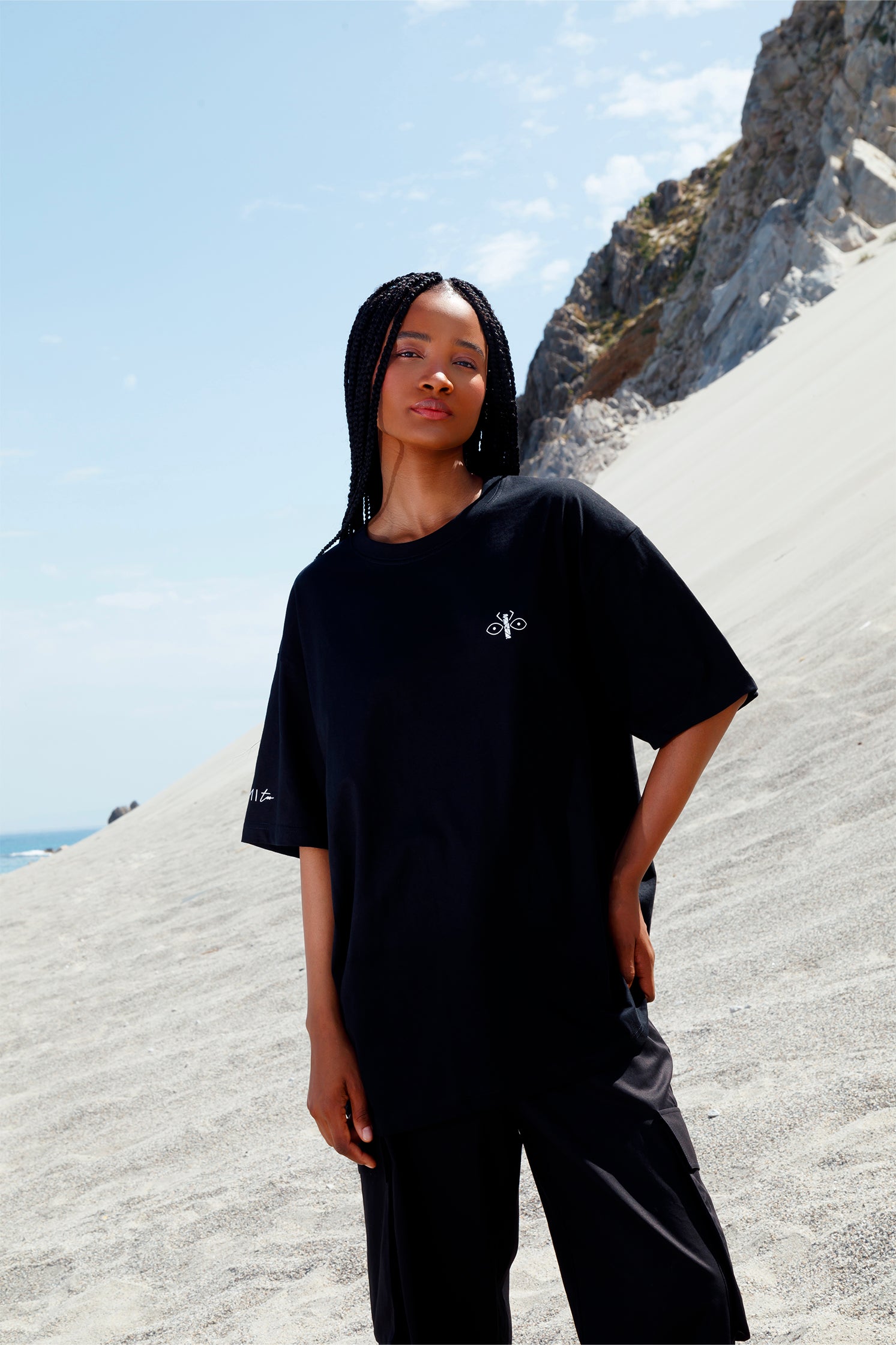 Black short-sleeved oversized unisex t-shirt worn by a model, featuring the scarab logo on the heart side and "Homi Too" printed on the right sleeve.