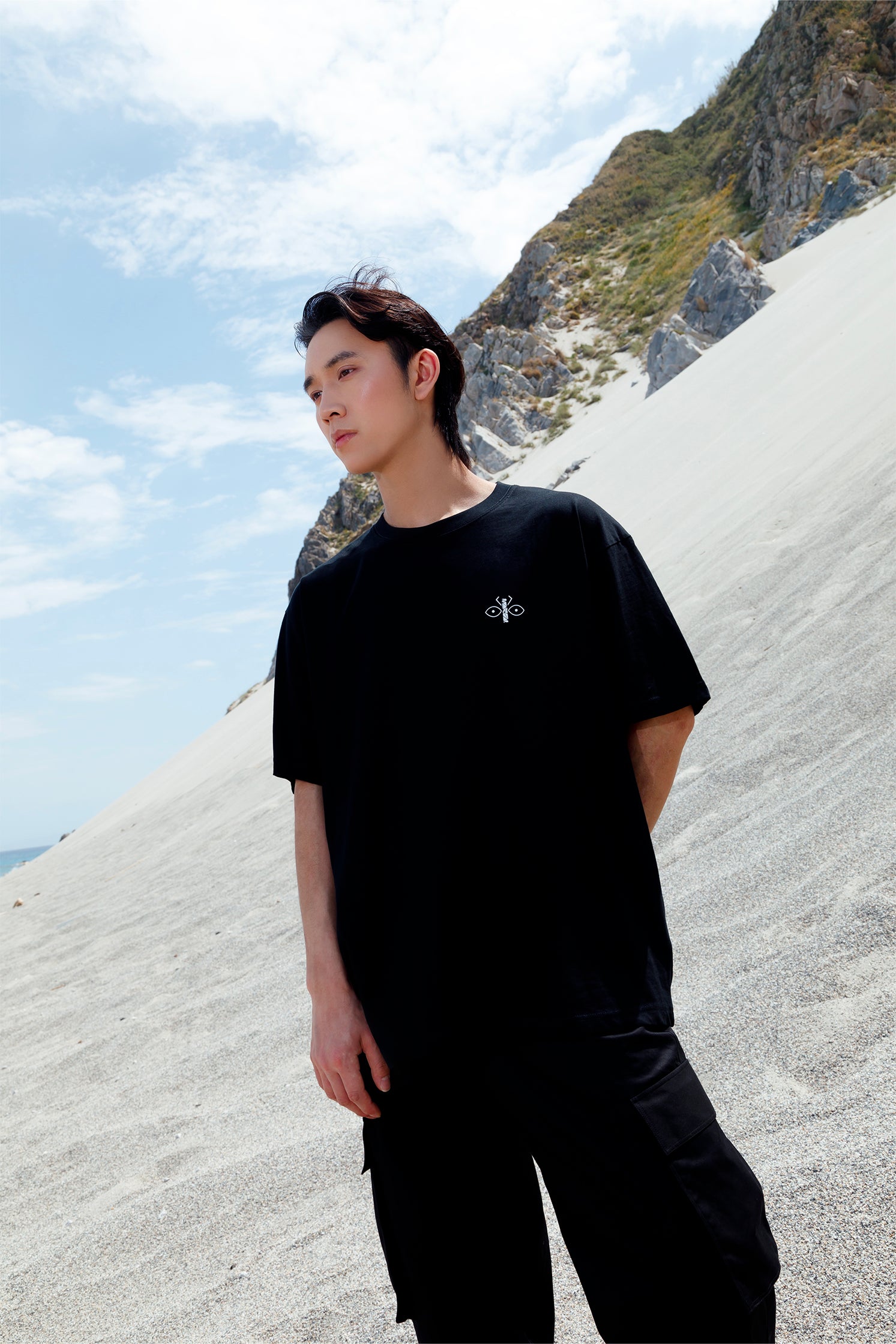 Black short-sleeved oversized unisex t-shirt worn by a model, featuring the scarab logo on the heart side and "Homi Too" printed on the right sleeve.