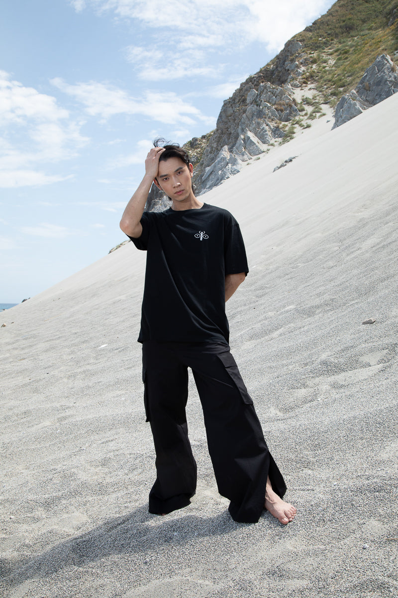 Black short-sleeved oversized unisex t-shirt worn by a model, featuring the scarab logo on the heart side and "Homi Too" printed on the right sleeve.