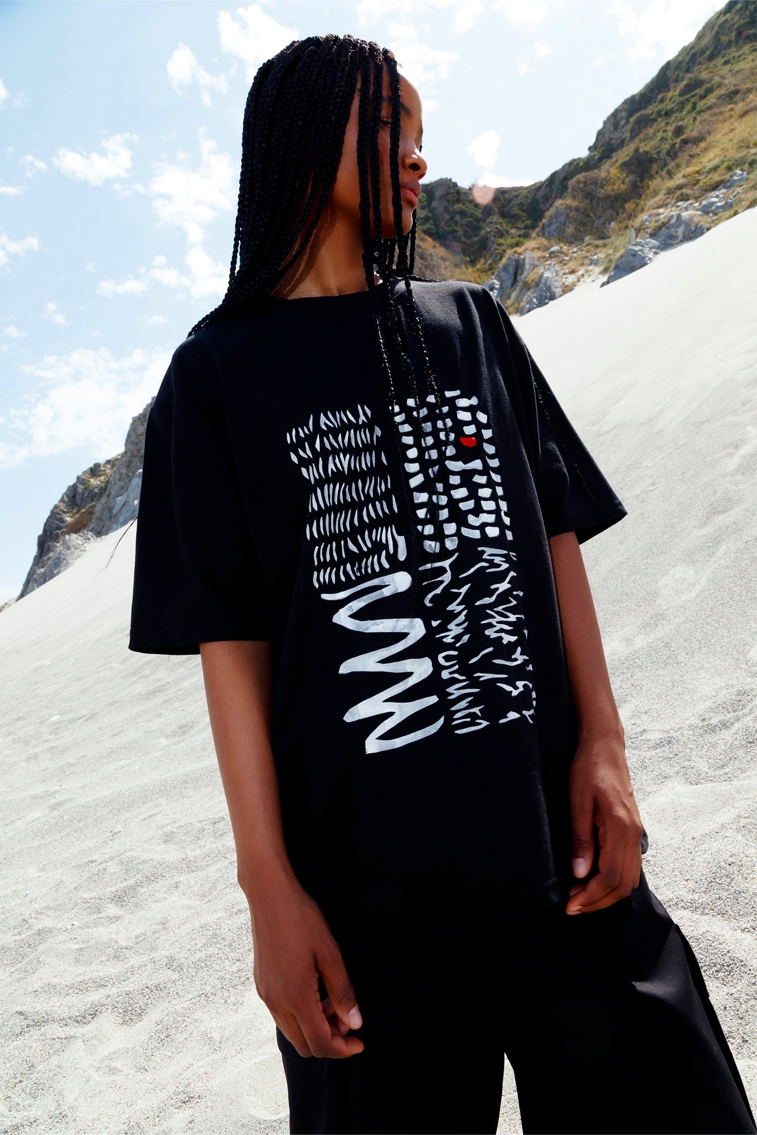 Black oversized unisex short-sleeved t-shirt worn by a model, featuring a hand-crafted abstract print on the front with white lines and a red detail in raised silicone.