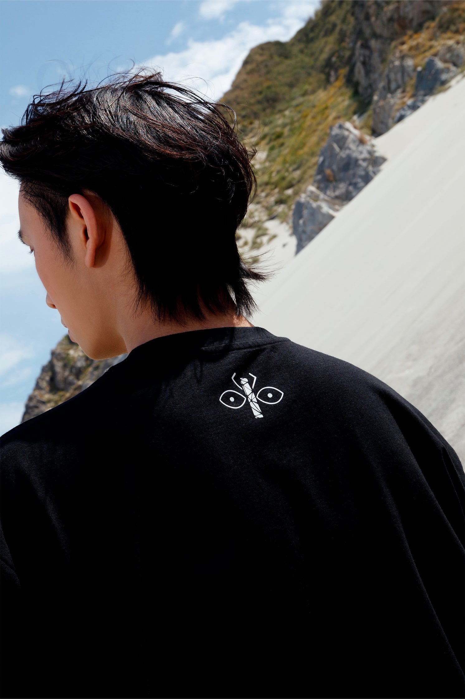 Back view of black oversized unisex t-shirt worn by a model, showing the white scarab logo printed just below the collar.