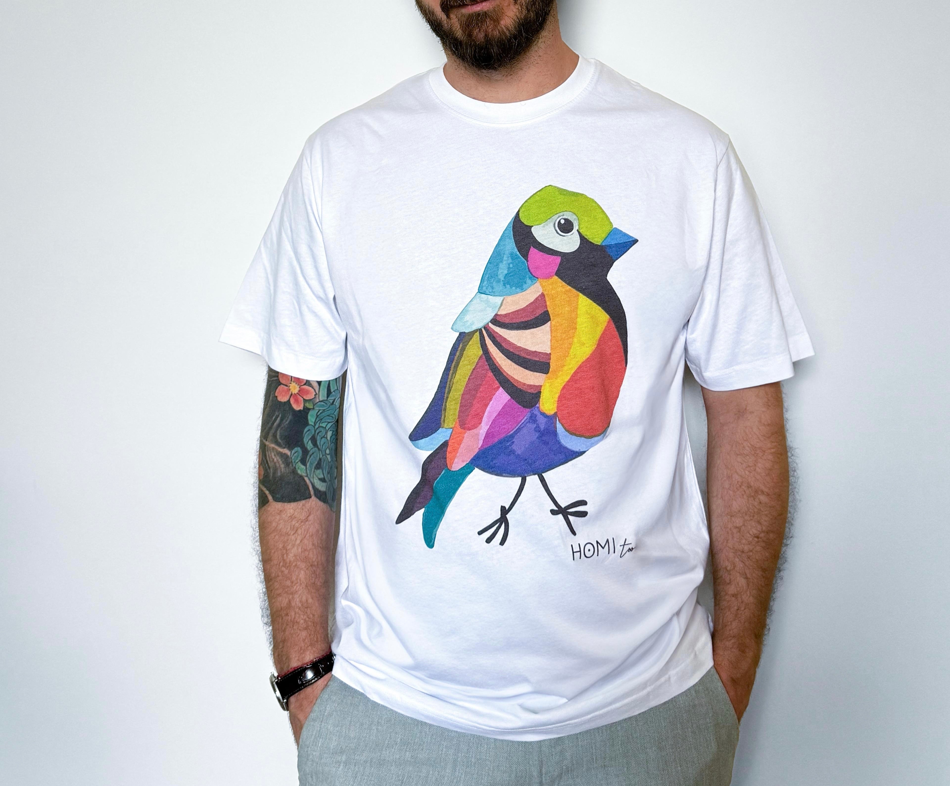 White oversized unisex t-shirt worn by a model, featuring a hand-painted colorful bird graphic on the front and "Homi Too" printed in small letters below the graphic on the left side.