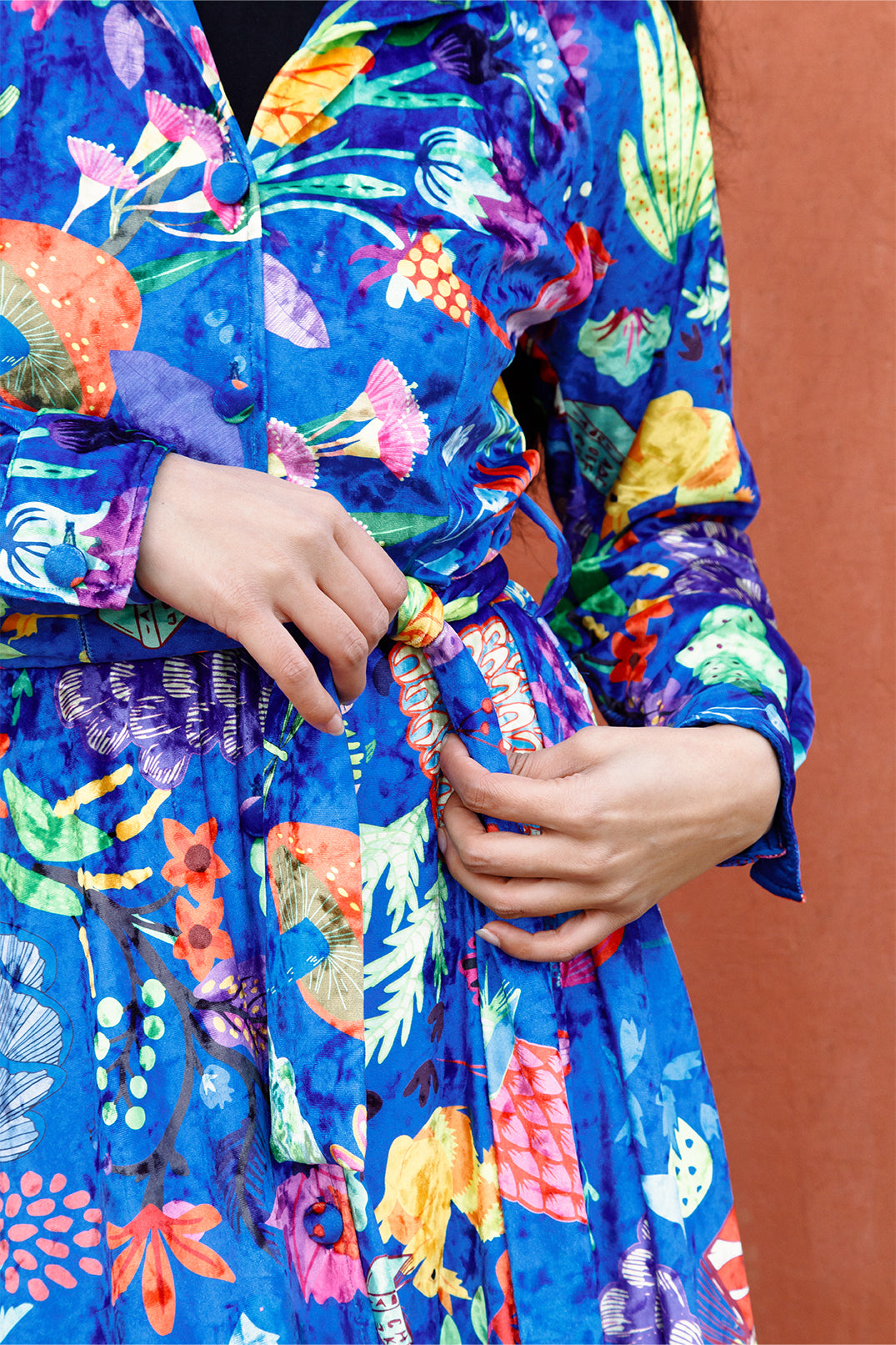 Close-up of the exclusive artistic graphic on the long blue velvet dress worn by a model, composed of drawings and vibrant colors.