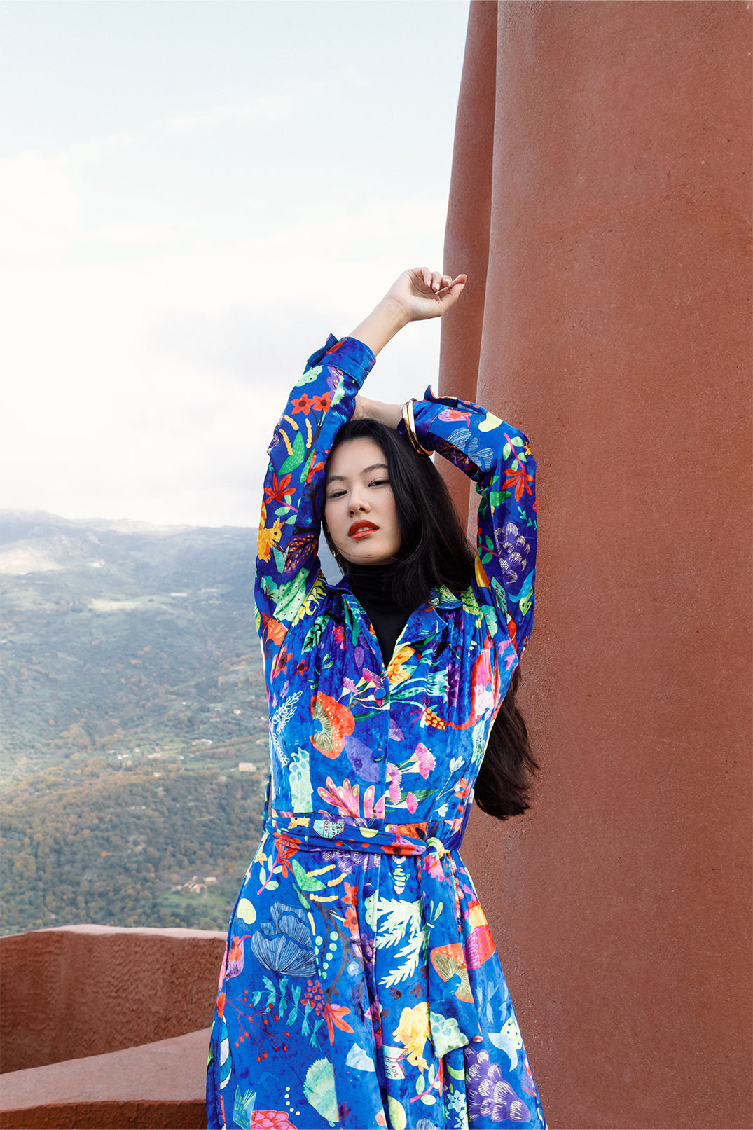 Close-up of the exclusive artistic graphic on the long blue velvet dress worn by a model, composed of drawings and vibrant colors.