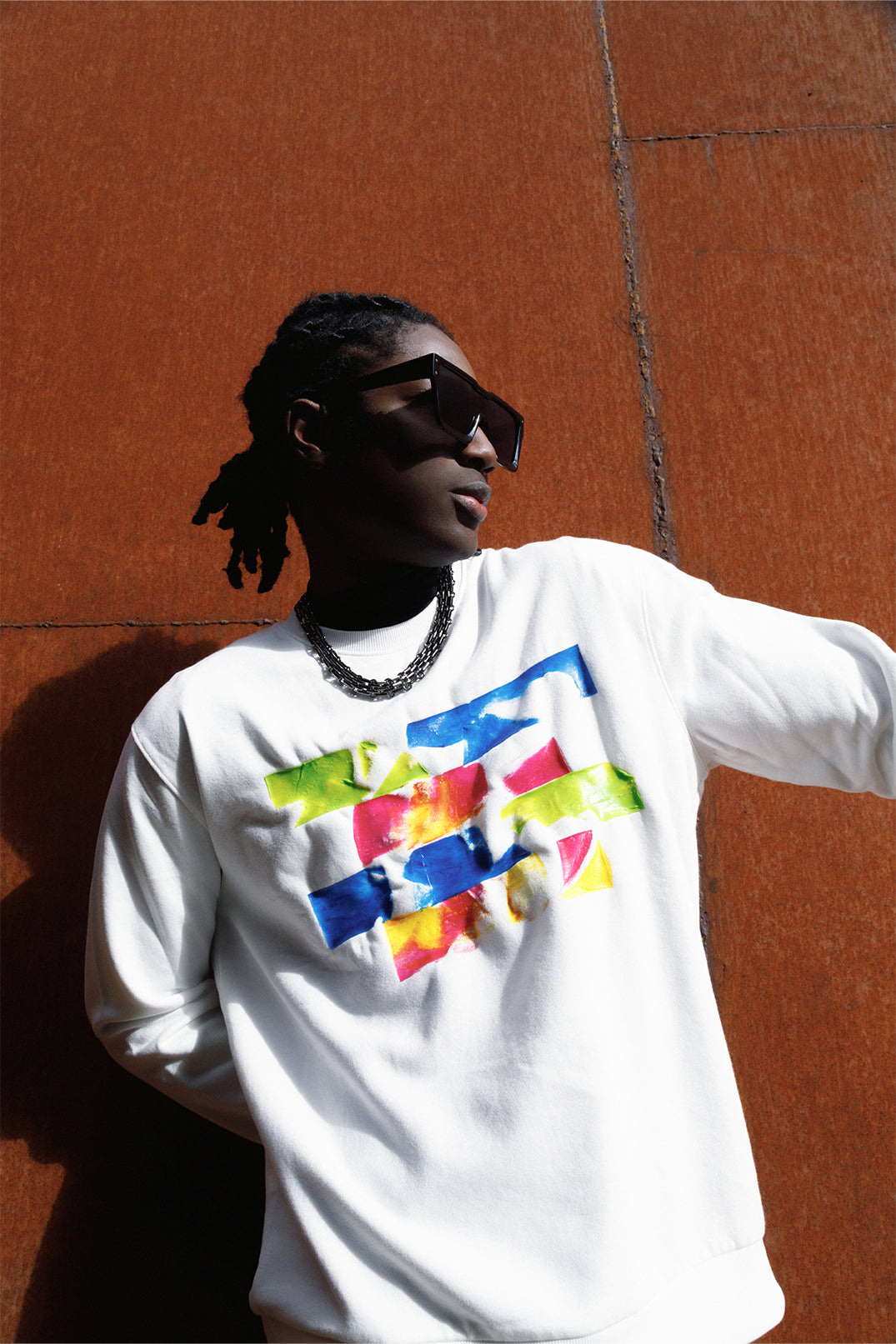 White oversized sweatshirt worn by a model, featuring a relaxed fit, long sleeves and a colorful silicon pattern on the chest.