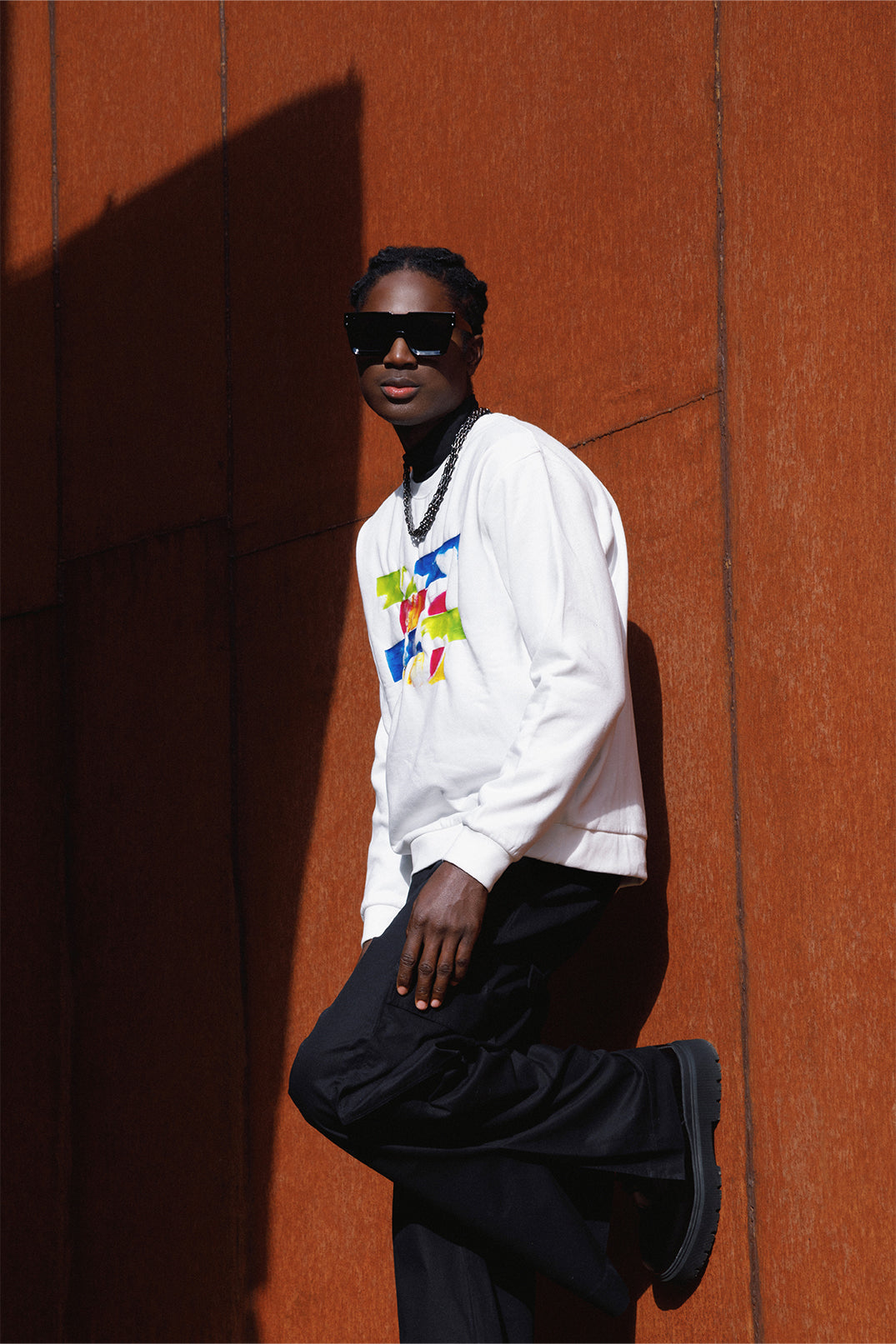 Side view of the white oversized sweatshirt worn by a model, featuring a relaxed fit, long sleeves and a colorful silicon pattern on the chest.