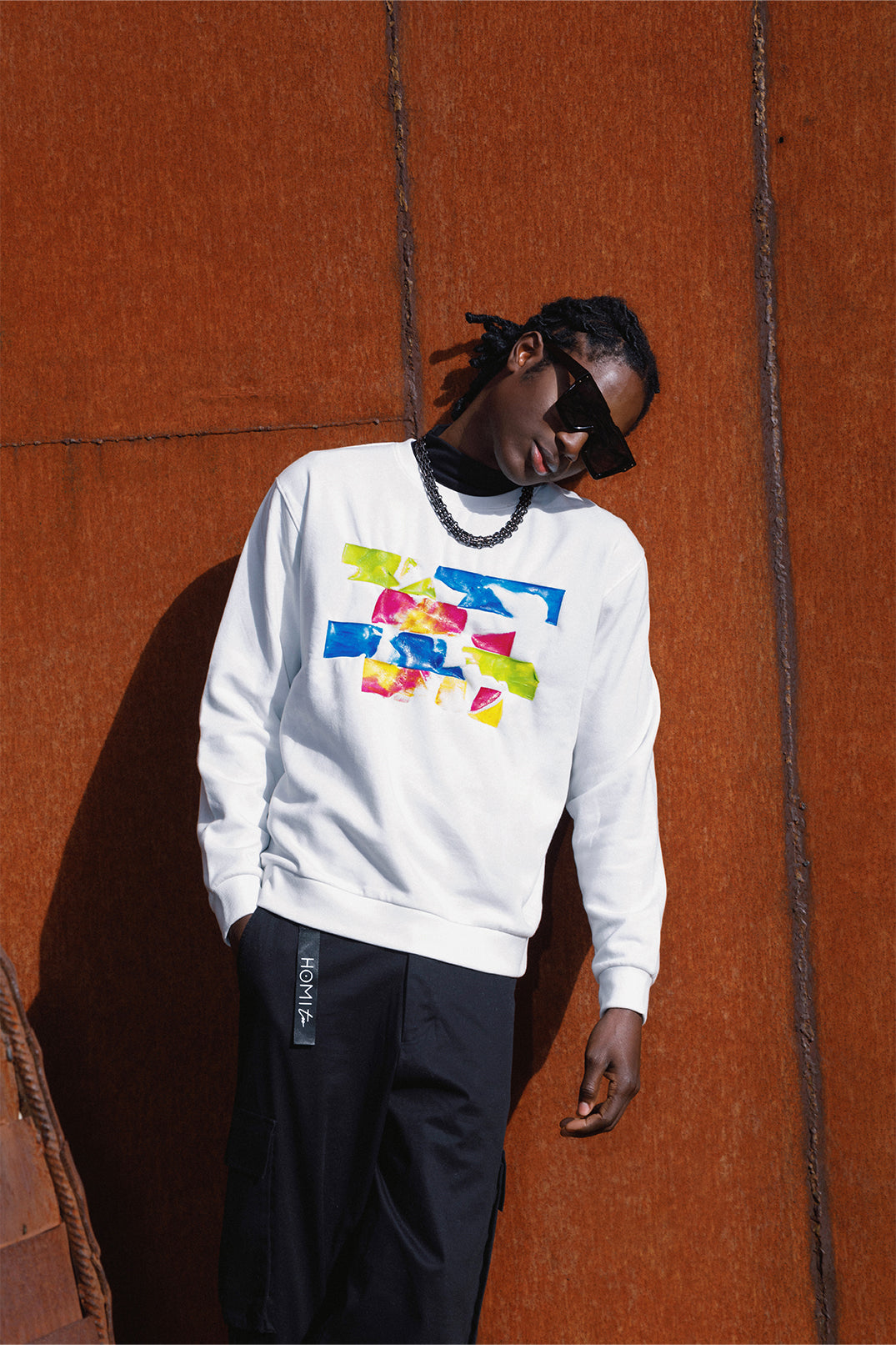 White oversized sweatshirt worn by a model, featuring a relaxed fit, long sleeves and a colorful silicon pattern on the chest.