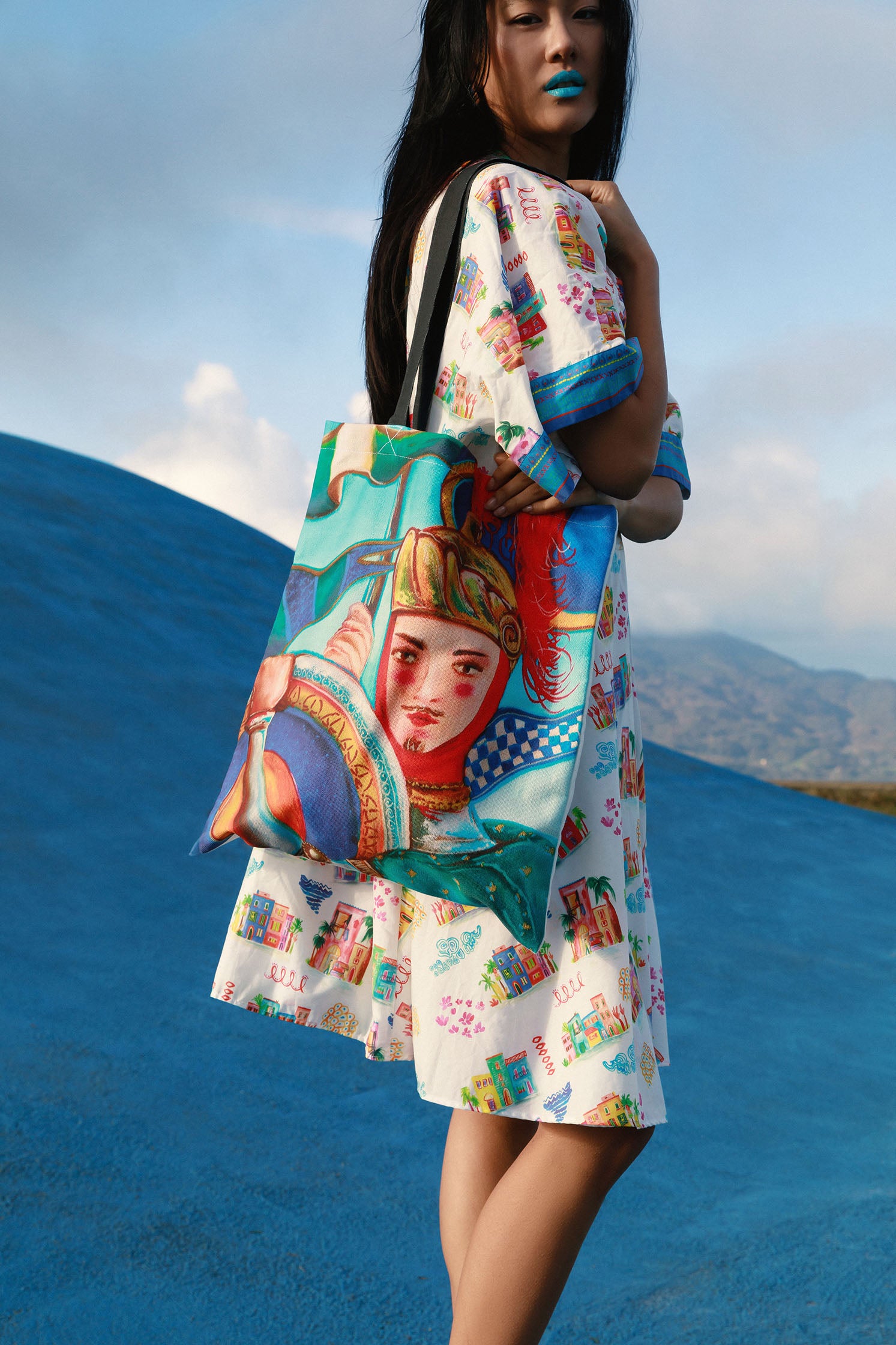 Natural cotton shopper bag featuring an exclusive "Sicilian Puppet" print derived from a hand-painted illustration, showing vibrant colors and refined details worn by a model.