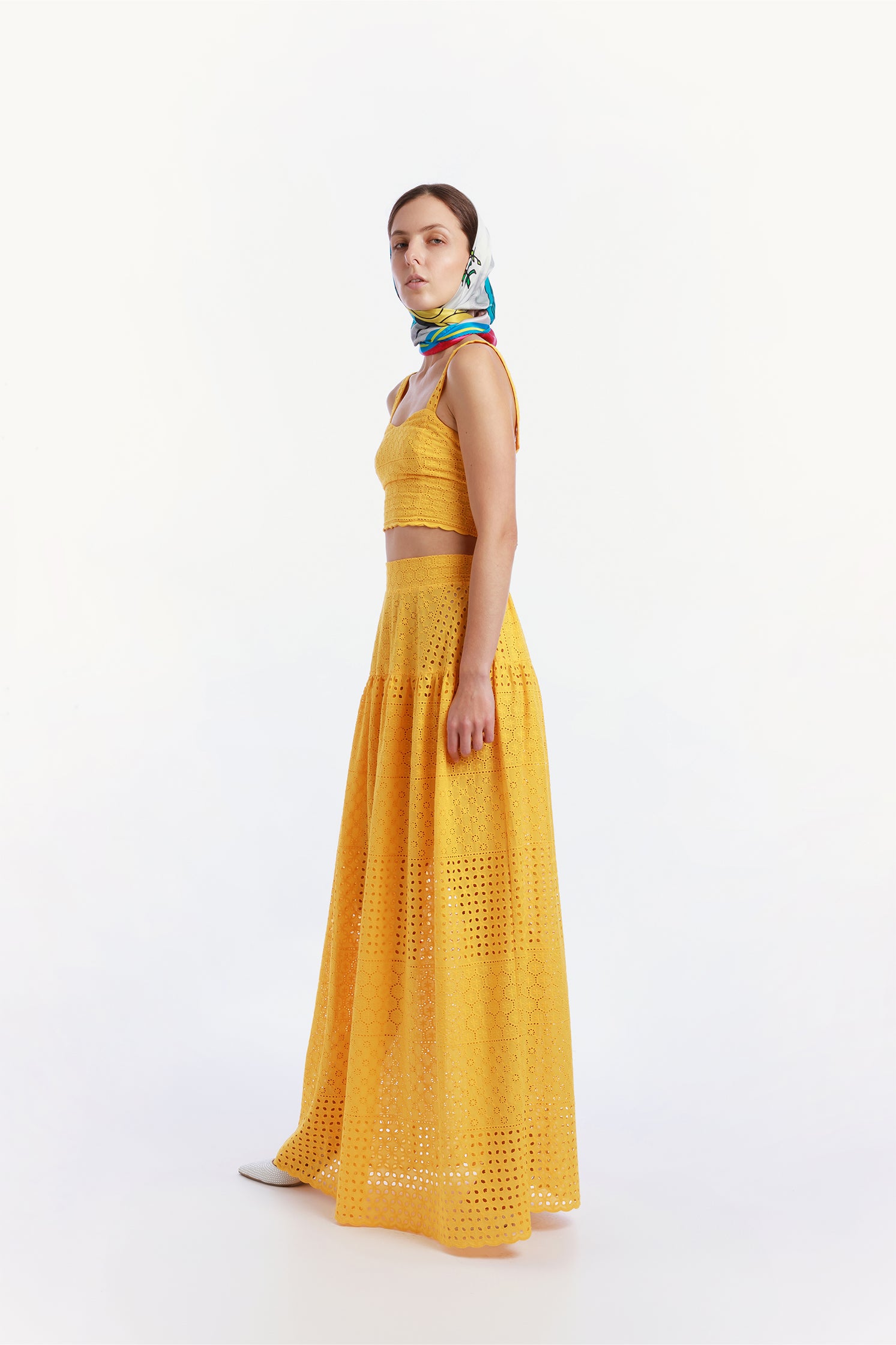 Side view of the pure silk scarf 90x90 cm worn around the head by a model, featuring a vibrant illustration of a Vespa in a colorful Sicilian landscape.