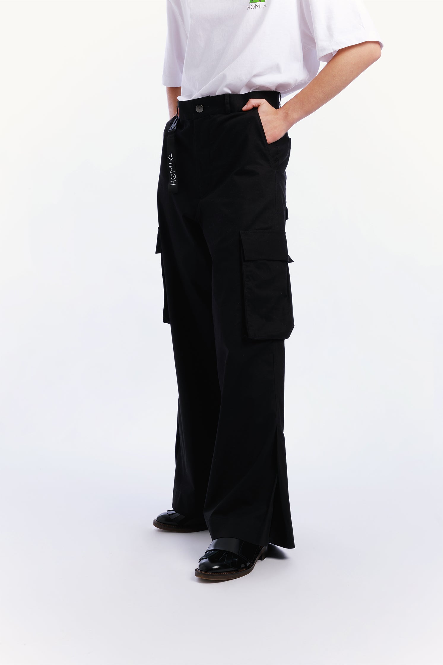 Unisex black cargo pants worn by a model with relaxed fit and side patch pockets, paired with a black keychain featuring the "Homi Too" logo in white lettering.