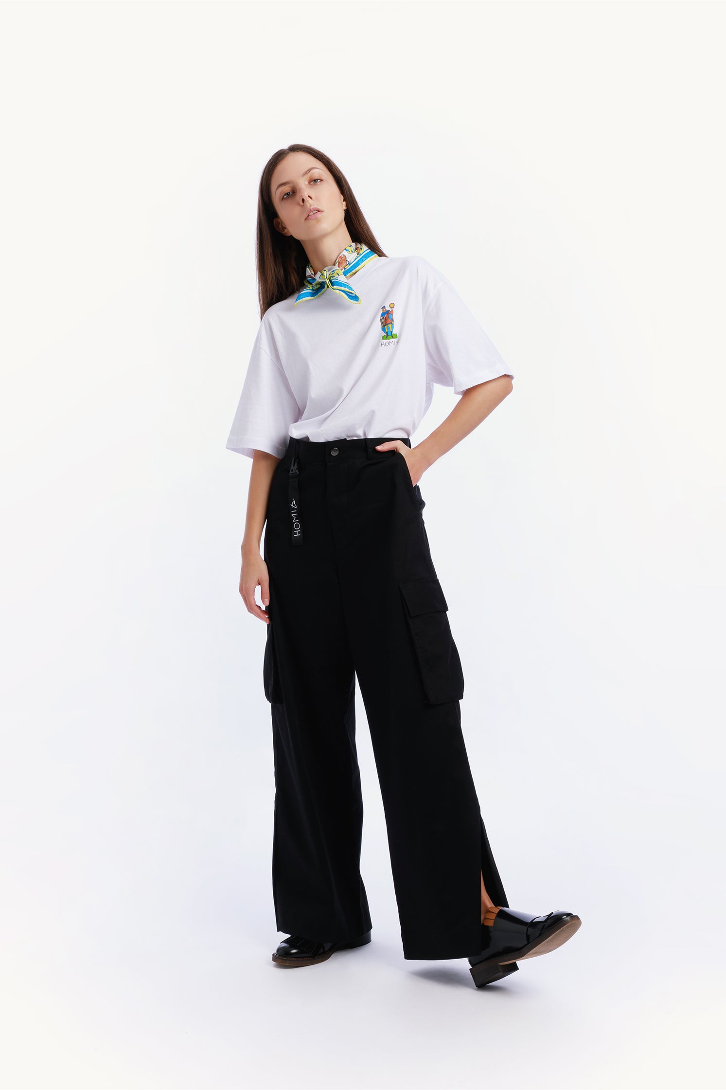 Unisex black cargo pants worn by a model with relaxed fit and side patch pockets, paired with a black keychain featuring the "Homi Too" logo in white lettering.