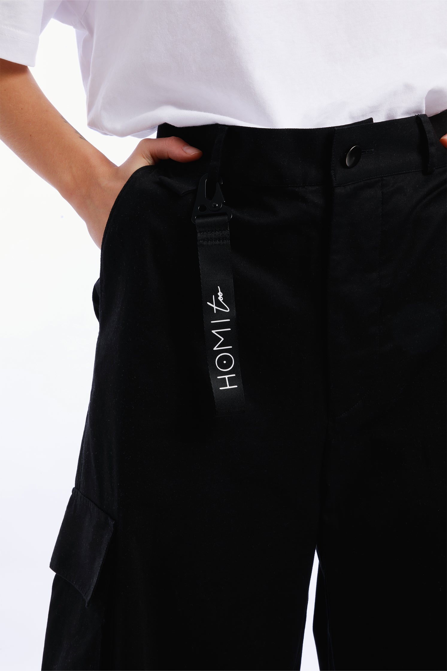 Close-up of the "Homi Too" logo on the black keychain, showing precise lettering and quality craftsmanship."