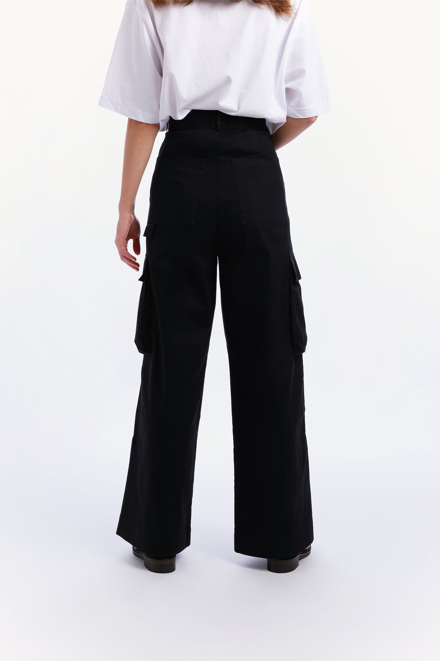 Back view of the unisex black cargo pants worn by a model with relaxed fit and side patch pockets.