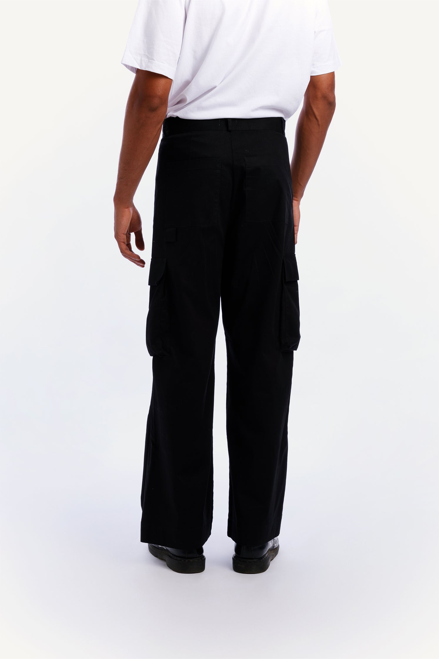Back view of the unisex black cargo pants worn by a model with relaxed fit and side patch pockets.