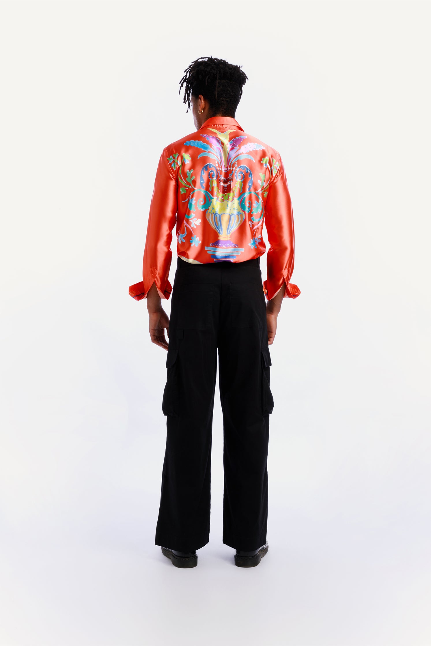 Back view of the unisex black cargo pants worn by a model with relaxed fit and side patch pockets.