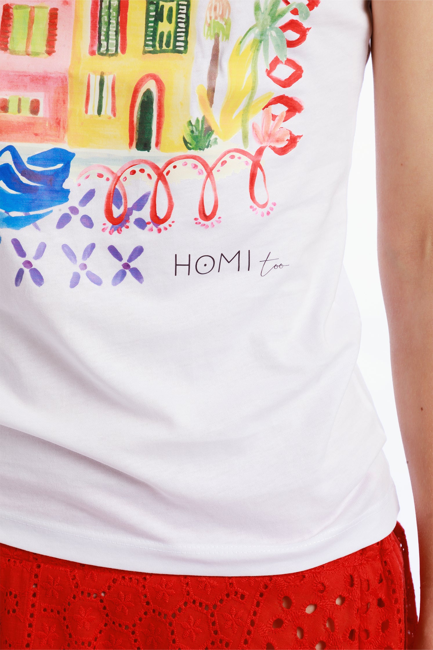 Close-up of the front graphic on the slim white T-shirt worn by a model, showing small colorful houses with intricate details and the "Homi Too" logo on the bottom let side.