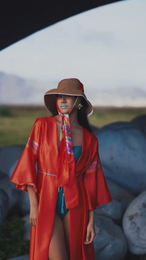 Long caftan worn by a model, featuring an exclusive all-over print on the back inspired by majolica tiles and artistic decorations, with vibrant colors on a satin orange base, wide sleeves and soft fit