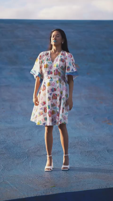 Wrap dress worn by a model, featuring a print of colorful Mediterranean houses, flattering wrap cut, kimono sleeves and lightweight flowing fabric