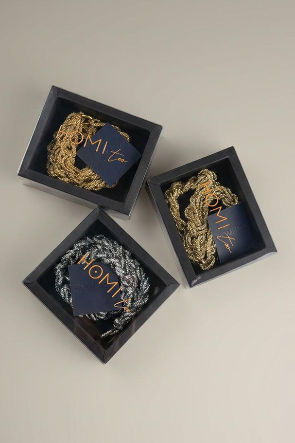 Gold and silver braided necklaces displayed in black gift boxes.