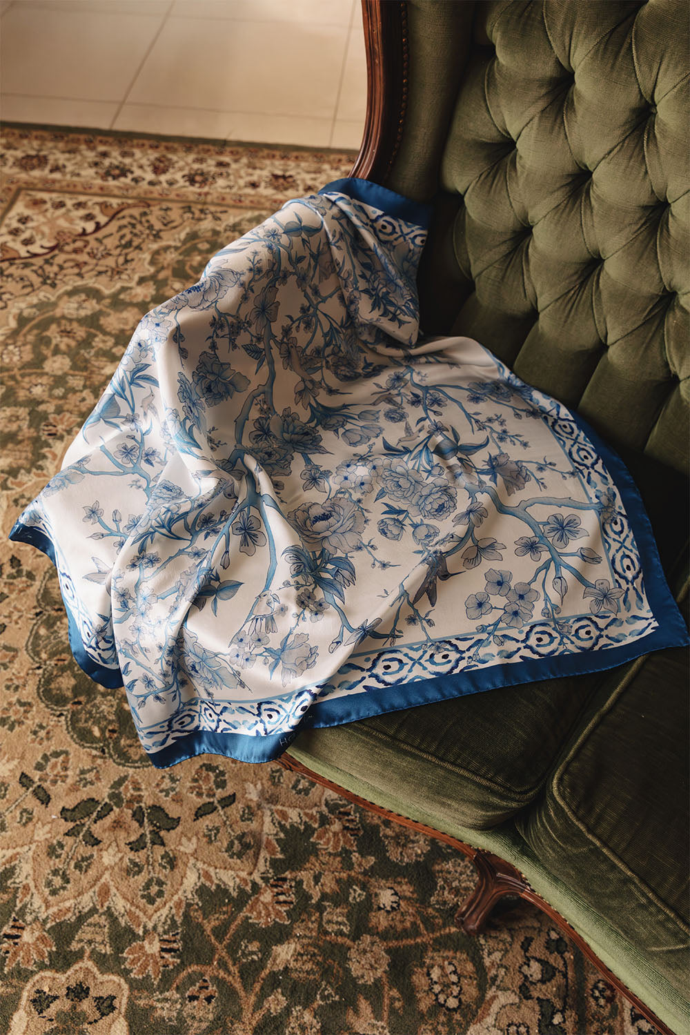 Blue and white floral silk scarf with a deep blue border and intricate botanical pattern featuring flowers, branches and leaves.