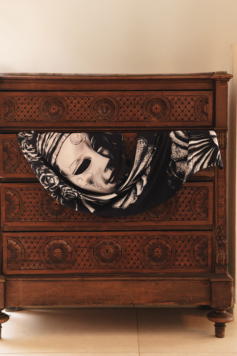 Silk scarf in black, featuring an intricate Venetian-inspired masked figure surrounded by sculptural floral and fan motifs in contrasting shades of white and gray.
