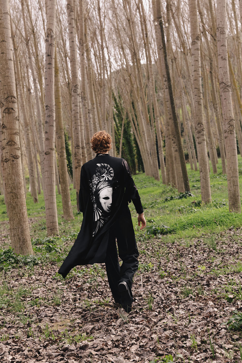 Black kimono worn by a model, featuring wide sleeves and a large black-and-white Venetian mask graphic on the back.