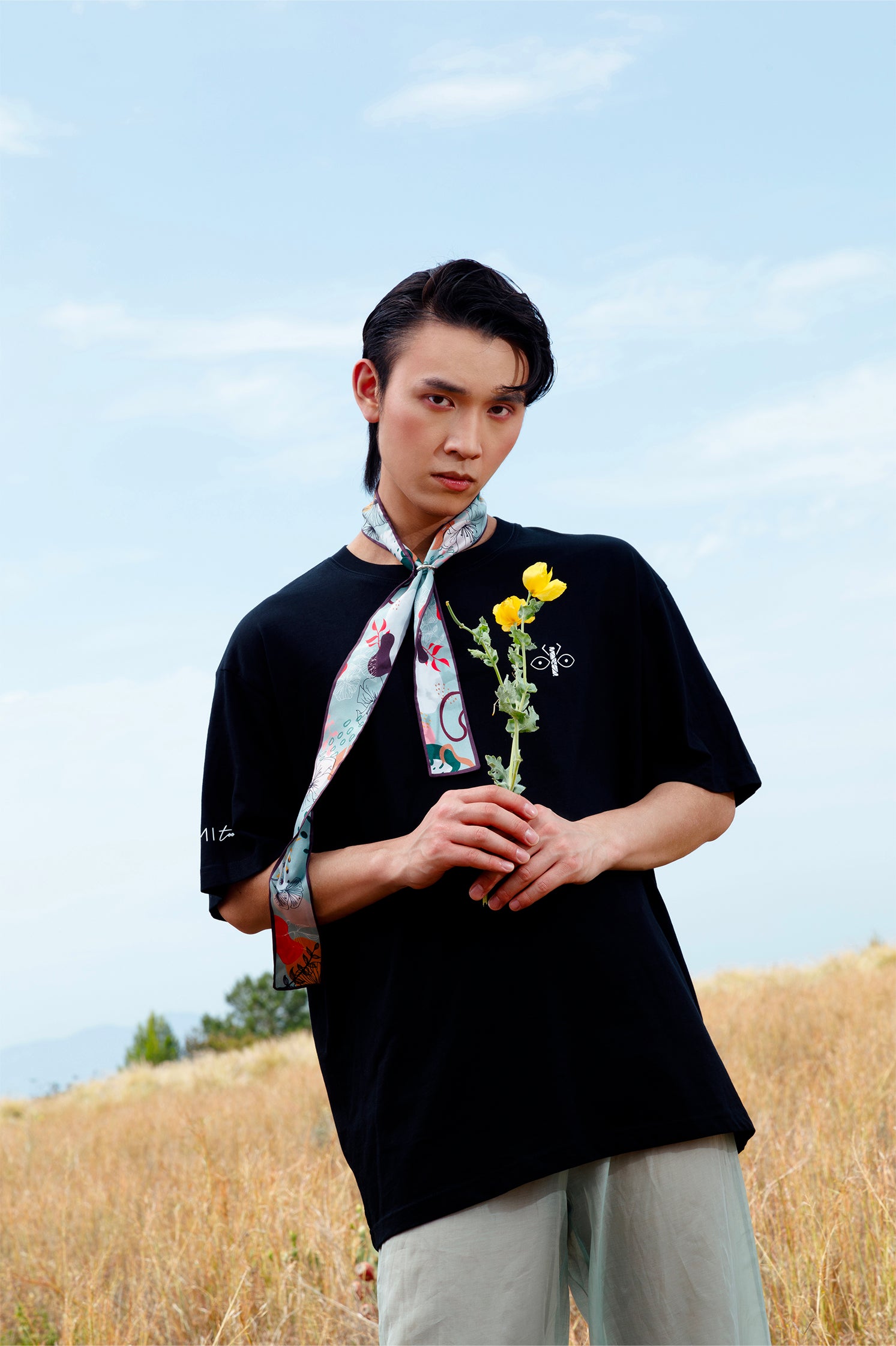 Silk scarf-tie in green and brown geometric pattern worn around the neck by a model, showing its slim and versatile format.