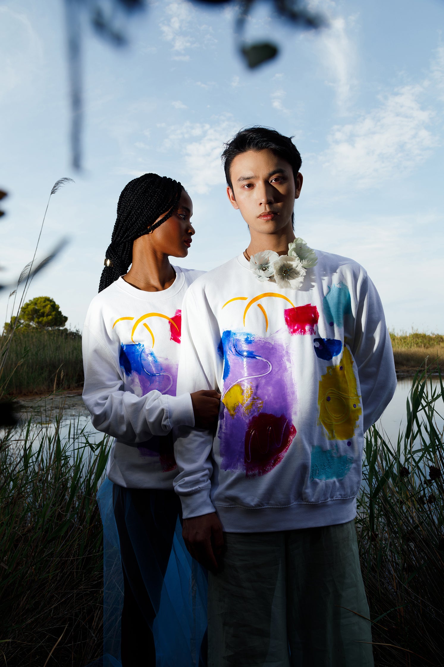 White oversized unisex sweatshirt worn by two models, showcasing the colorful abstract relief silicone print on the front, highlighting uniqueness and vibrant design.