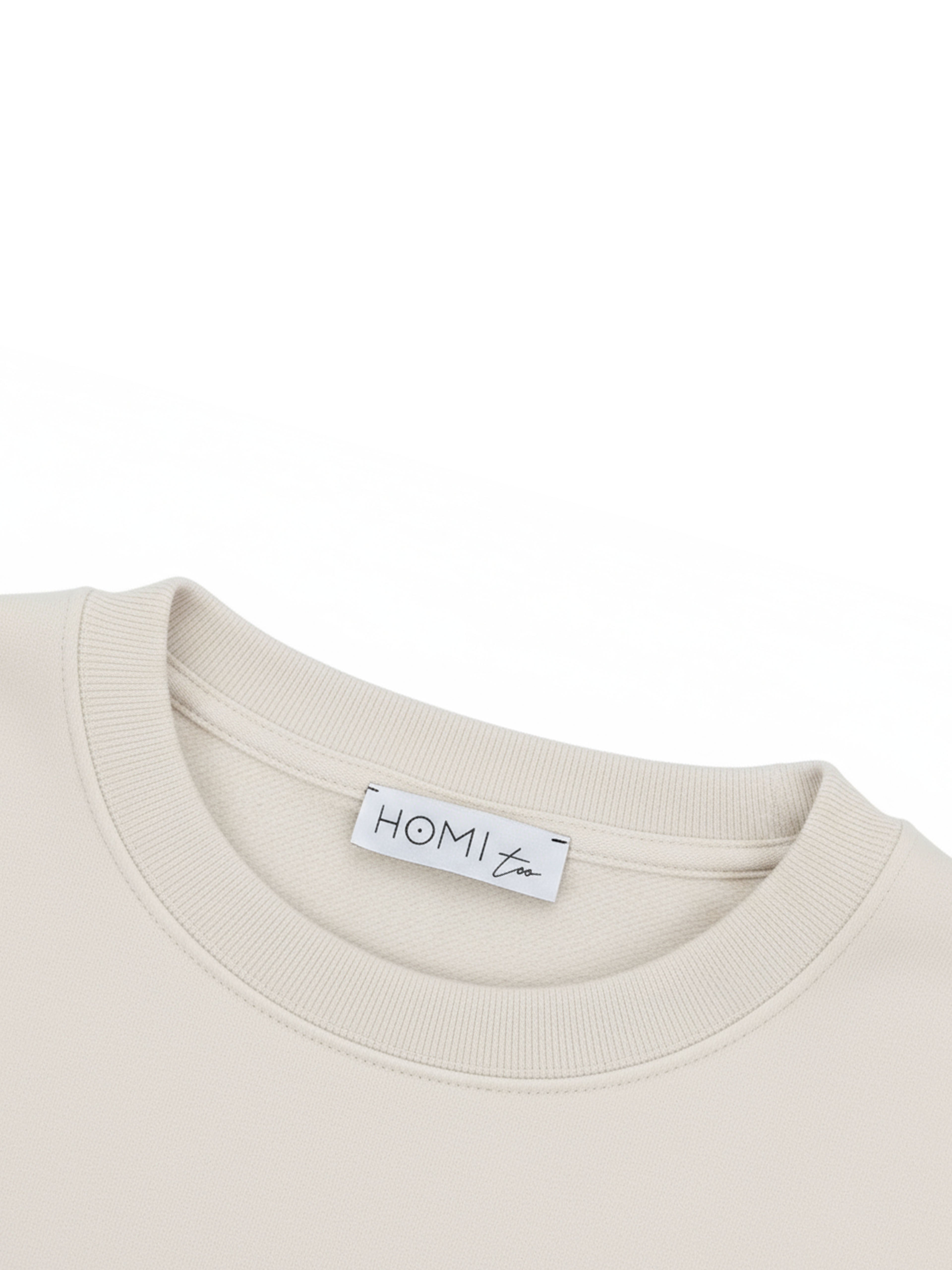 Close-up of the HOMI TOO logo label sewn on the back neckline of the sweatshirt.