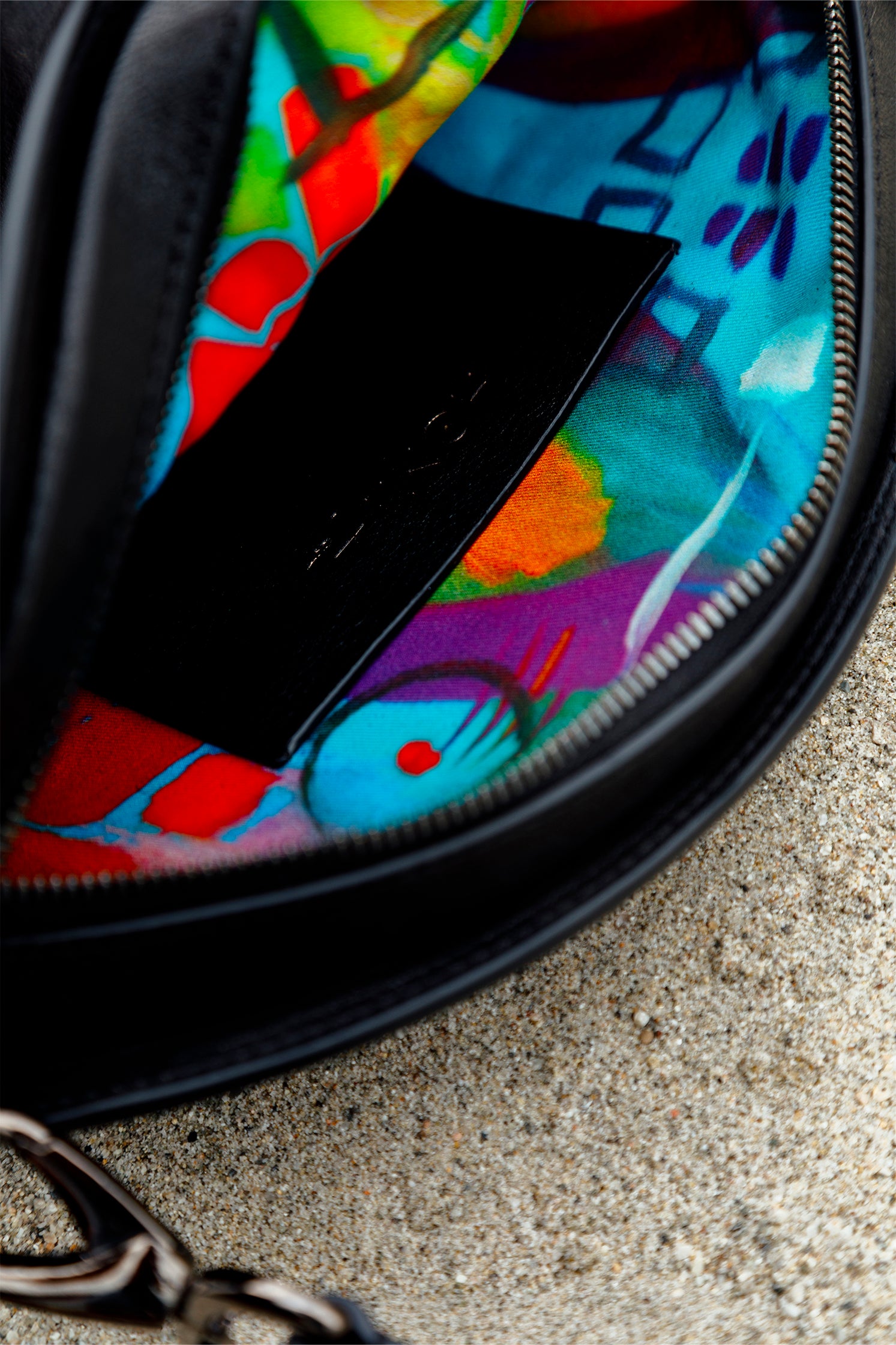 Interior close-up of the eye-shaped black leather bag, showing the colorful printed lining with vibrant artistic details