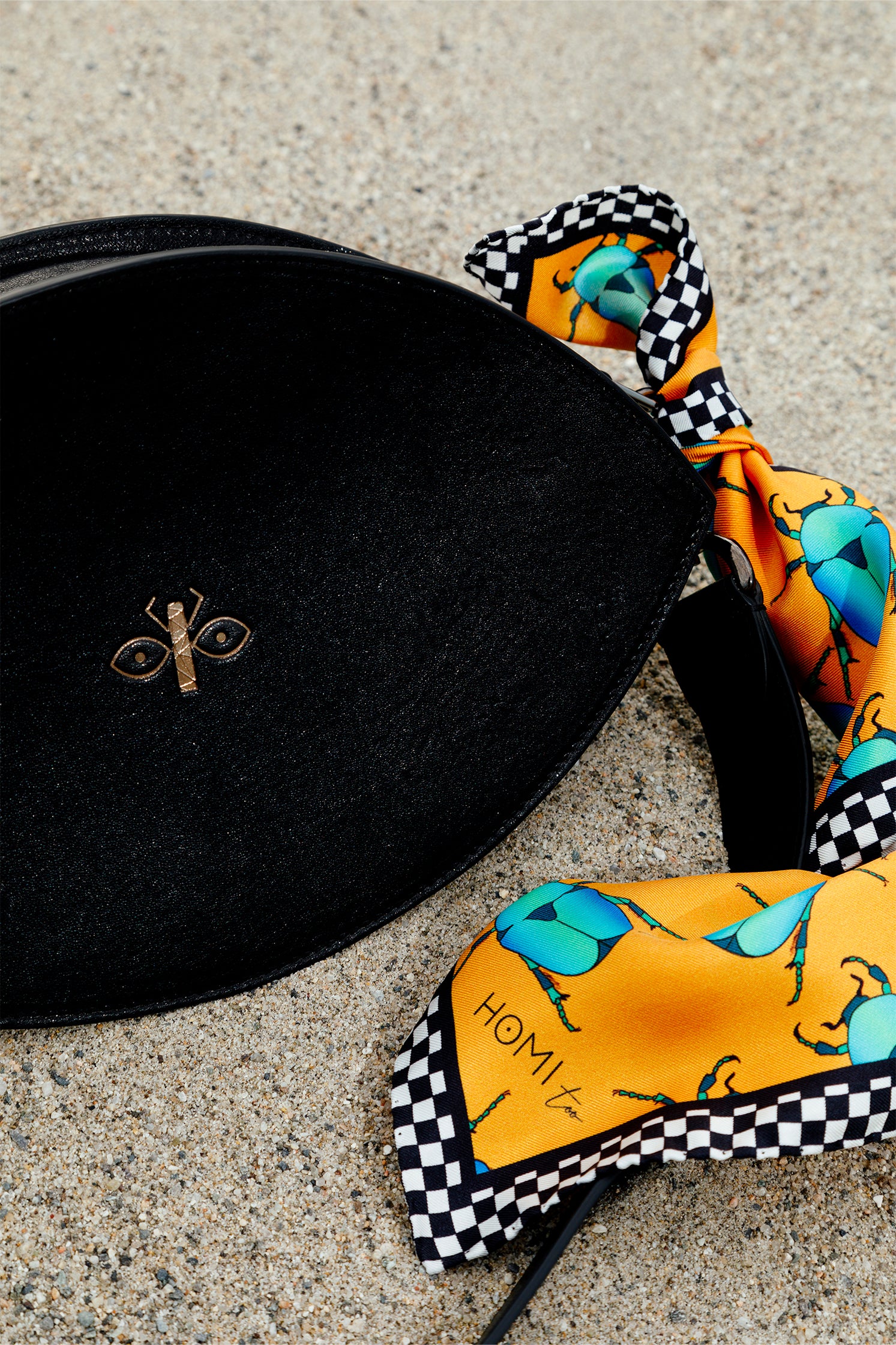Close-up of the black leather eye-shaped bag with engraved scarab logo, styled with a silk scarf tied to the handle