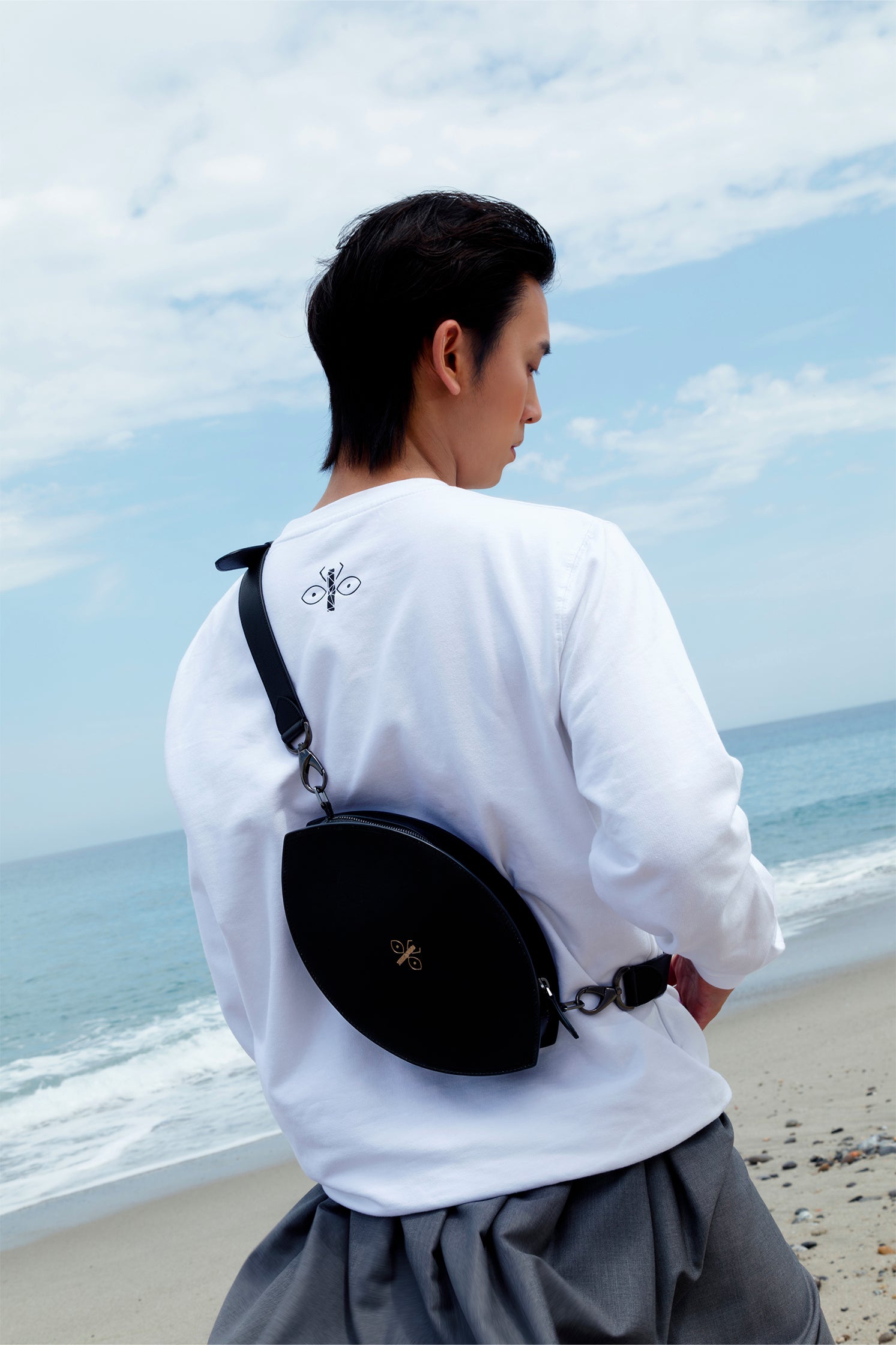 Eye-shaped black leather bag with engraved scarab logo worn by a model, showing its unique silhouette and chic style