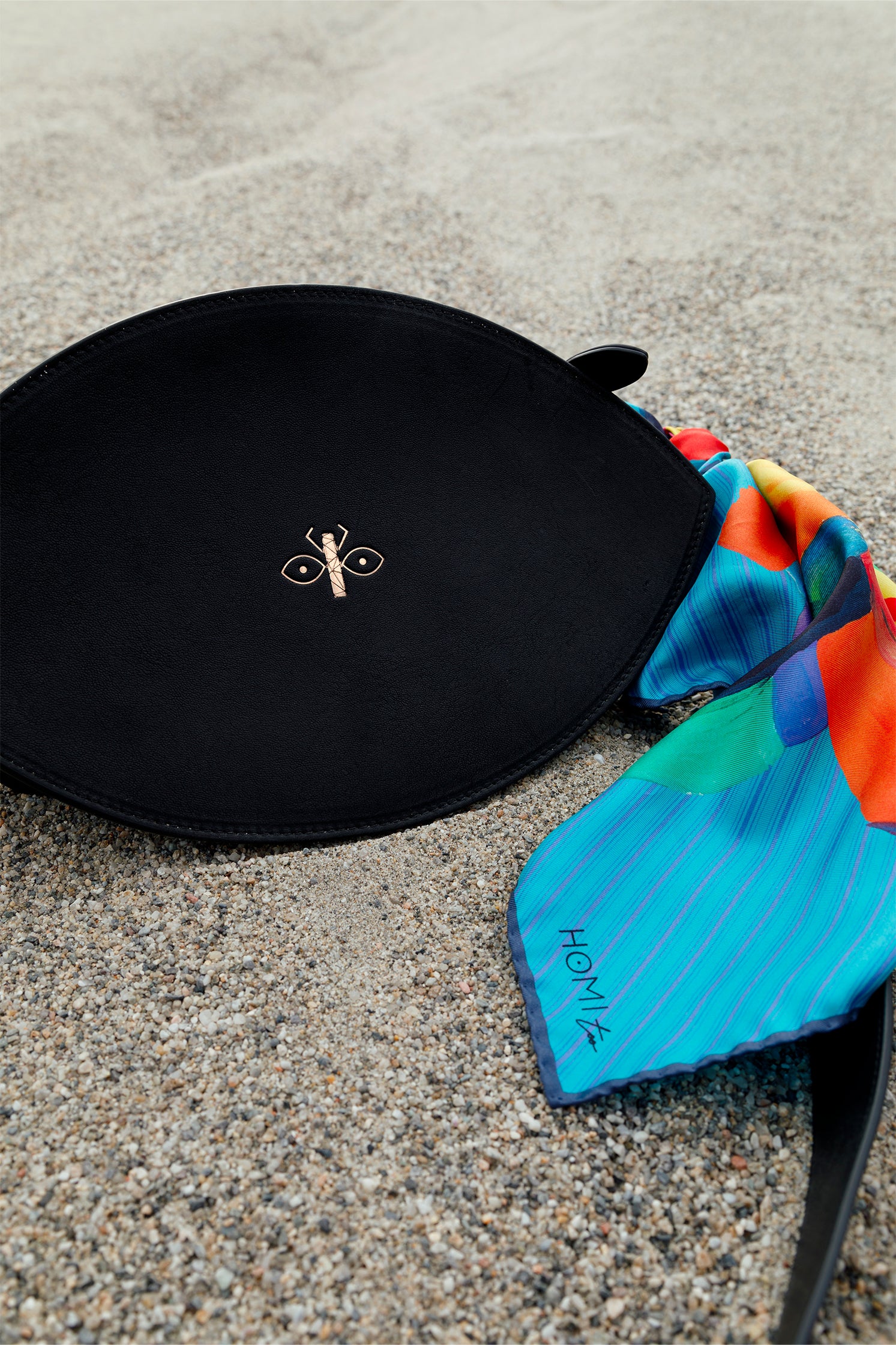 Silk scarf tied to a bag, showcasing multicolor geometric print on a blue-toned base, used as a stylish accessory.