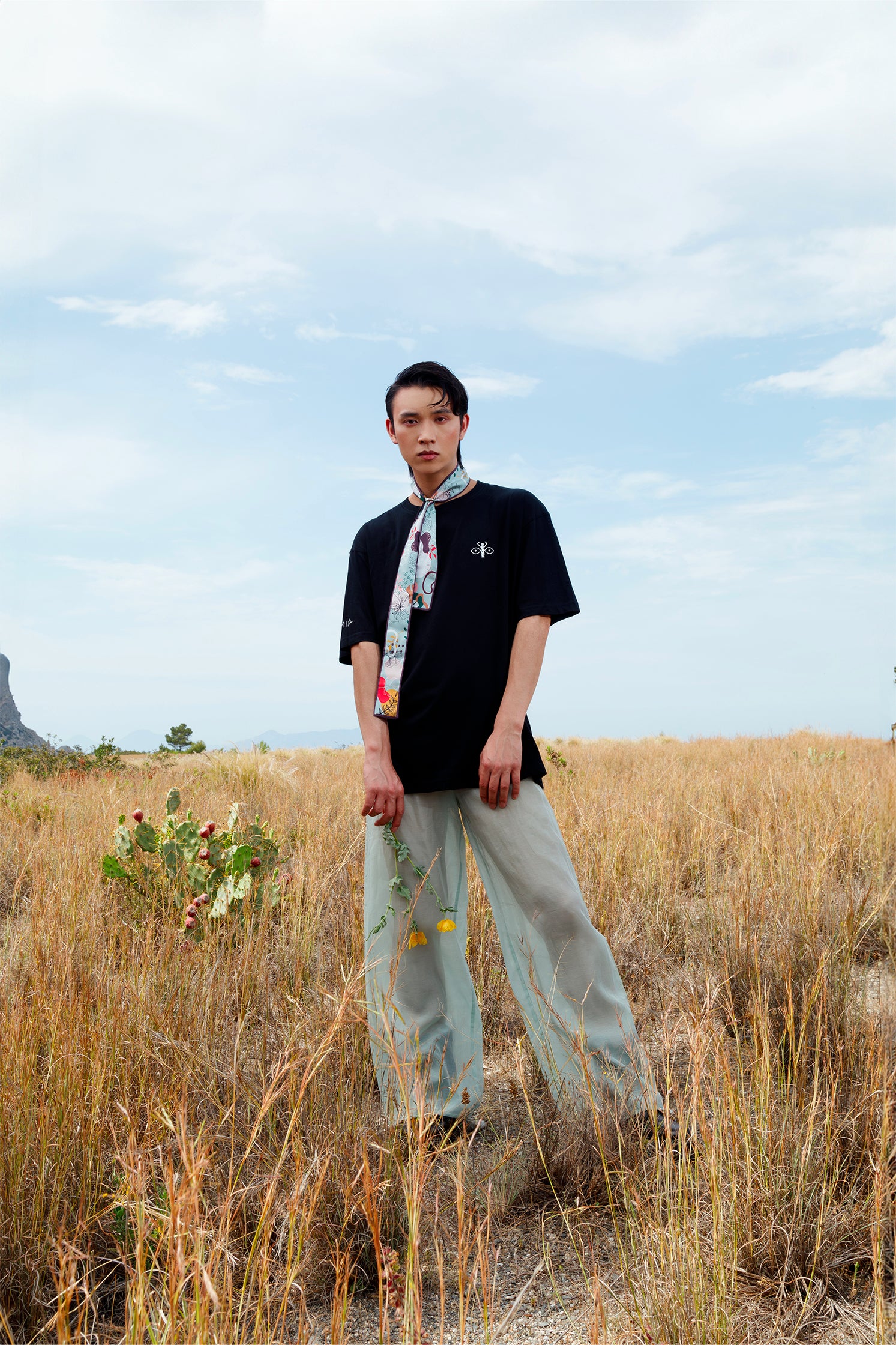 Silk scarf-tie in green and brown geometric pattern worn around the neck by a model, showing its slim and versatile format.