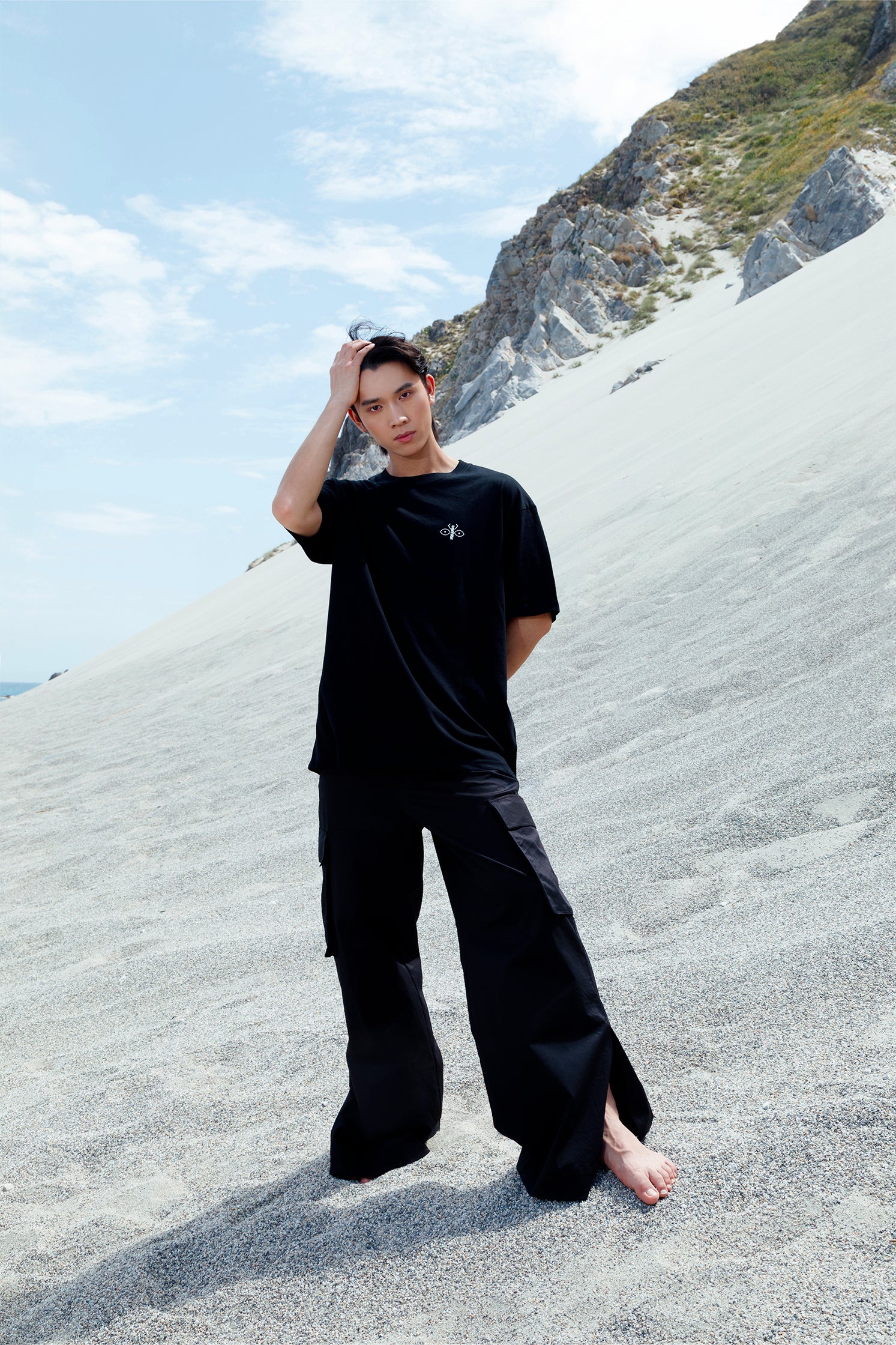 Unisex black cotton cargo pants worn by a model, featuring side patch pockets, relaxed fit, and small slit at the hem for added style and comfort.