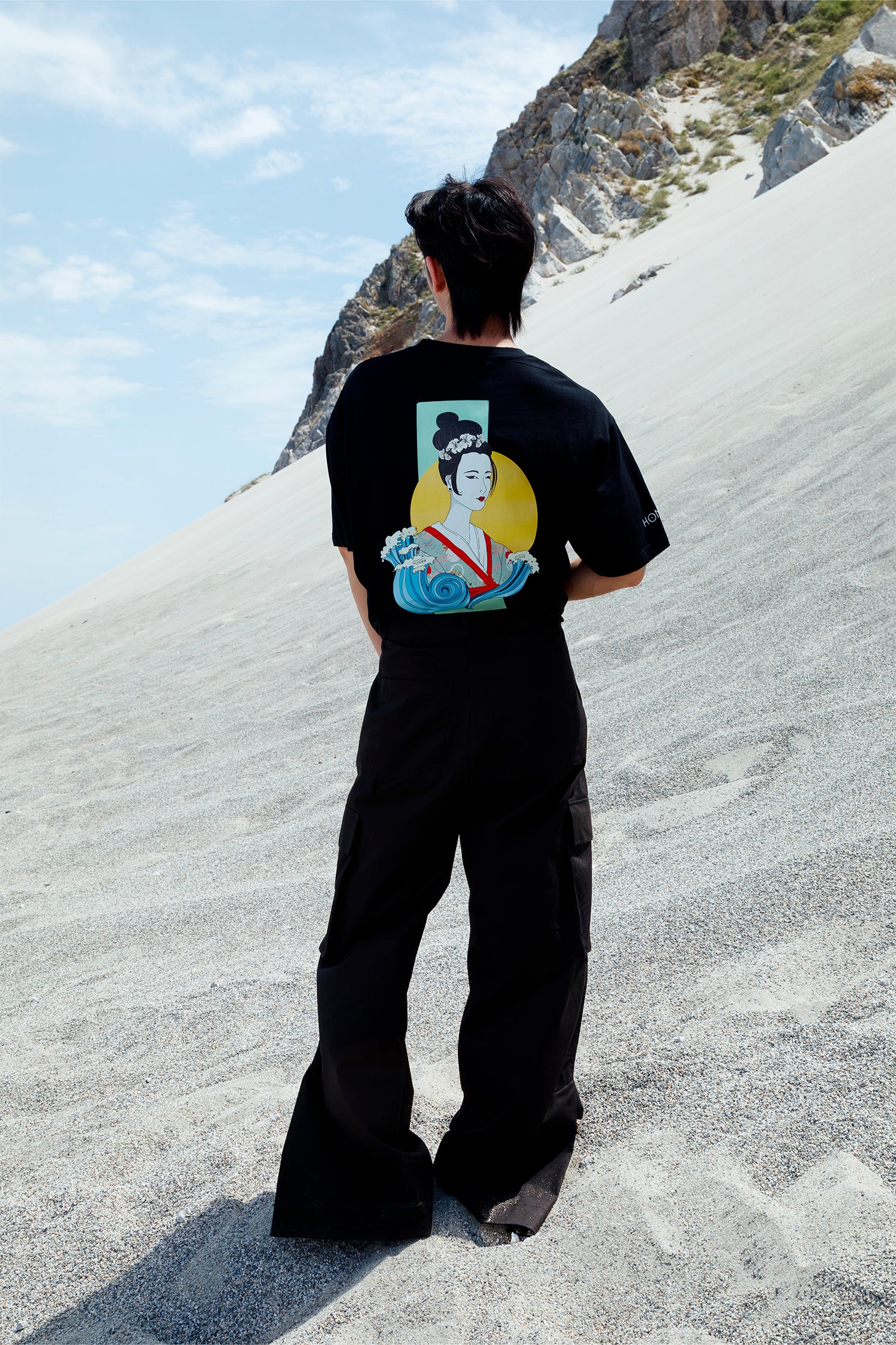 Back view of the unisex black cotton cargo pants worn by a model, featuring side patch pockets, relaxed fit, and small slit at the hem for added style and comfort.