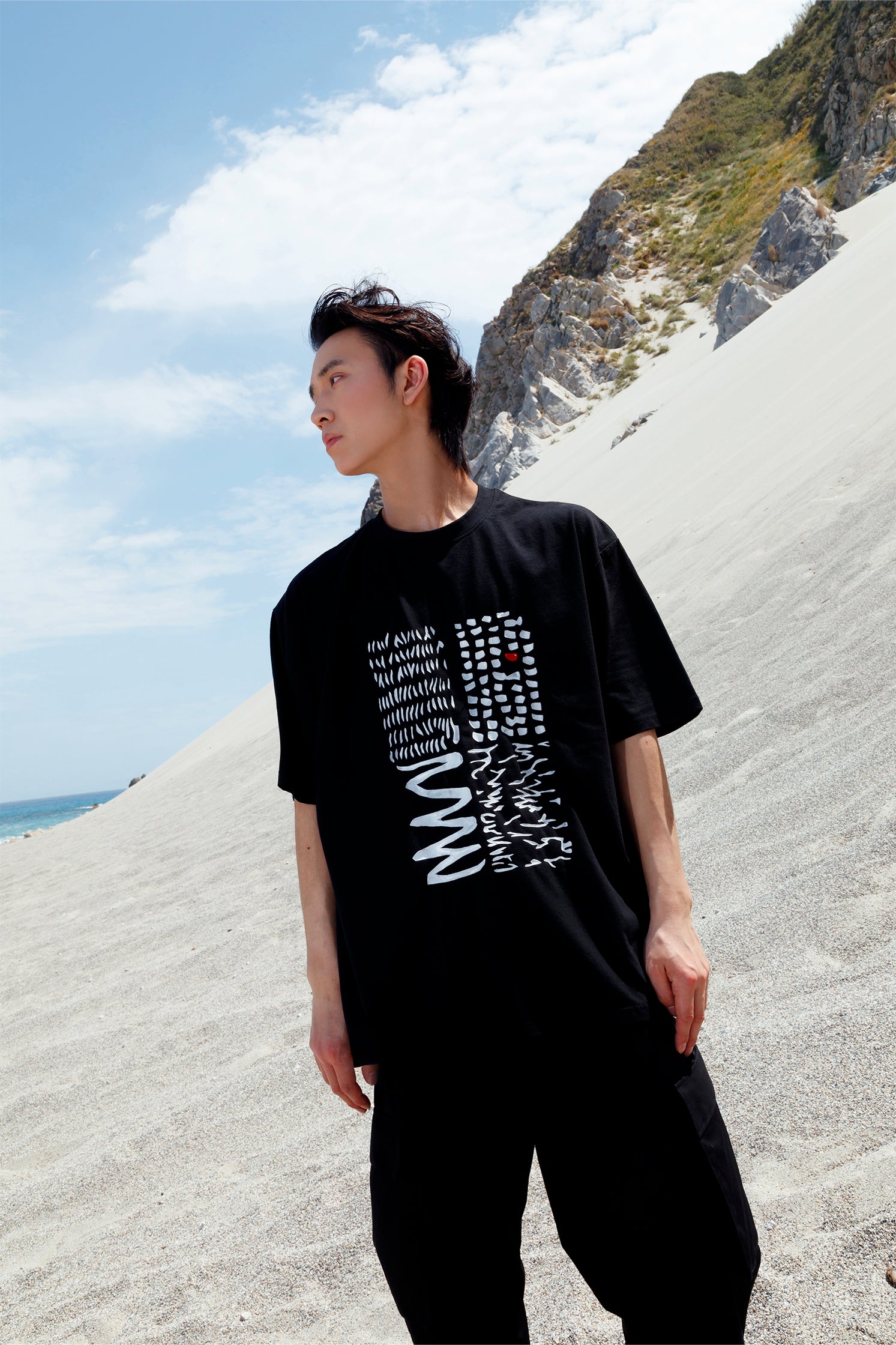 Black oversized unisex short-sleeved t-shirt worn by a model, featuring a hand-crafted abstract print on the front with white lines and a red detail in raised silicone.
