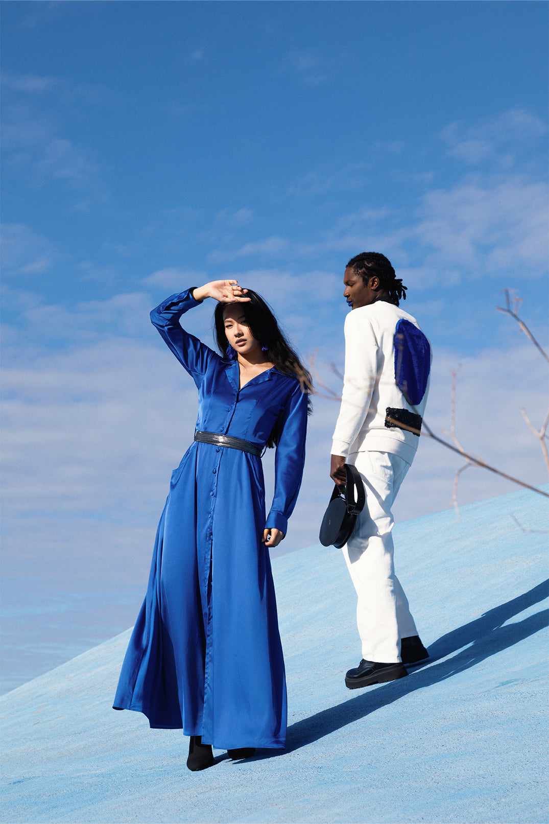 Elegant long royal blue dress worn by a model, with fluid silhouette, shirt collar, long sleeves.