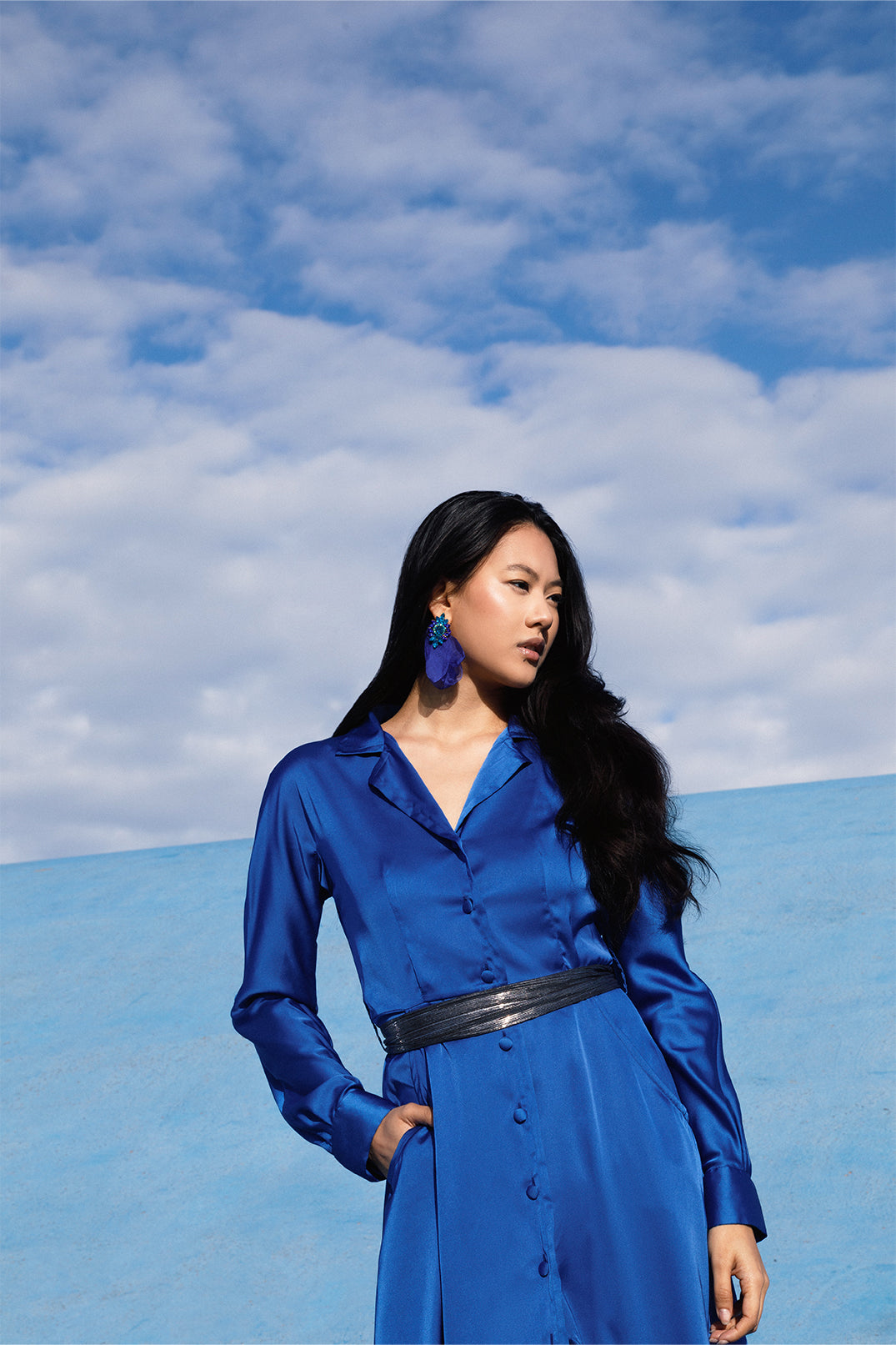 Close-up of the upper part of the elegant long royal blue dress worn by a model, with fluid silhouette, shirt collar, long sleeves.