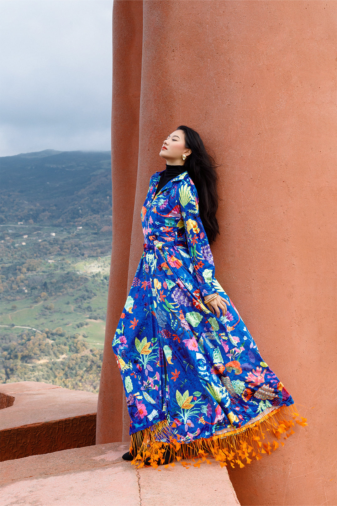 Long blue velvet dress worn by a model, featuring an exclusive artistic graphic, shirt collar, long sleeves, and fluid silhouette.
