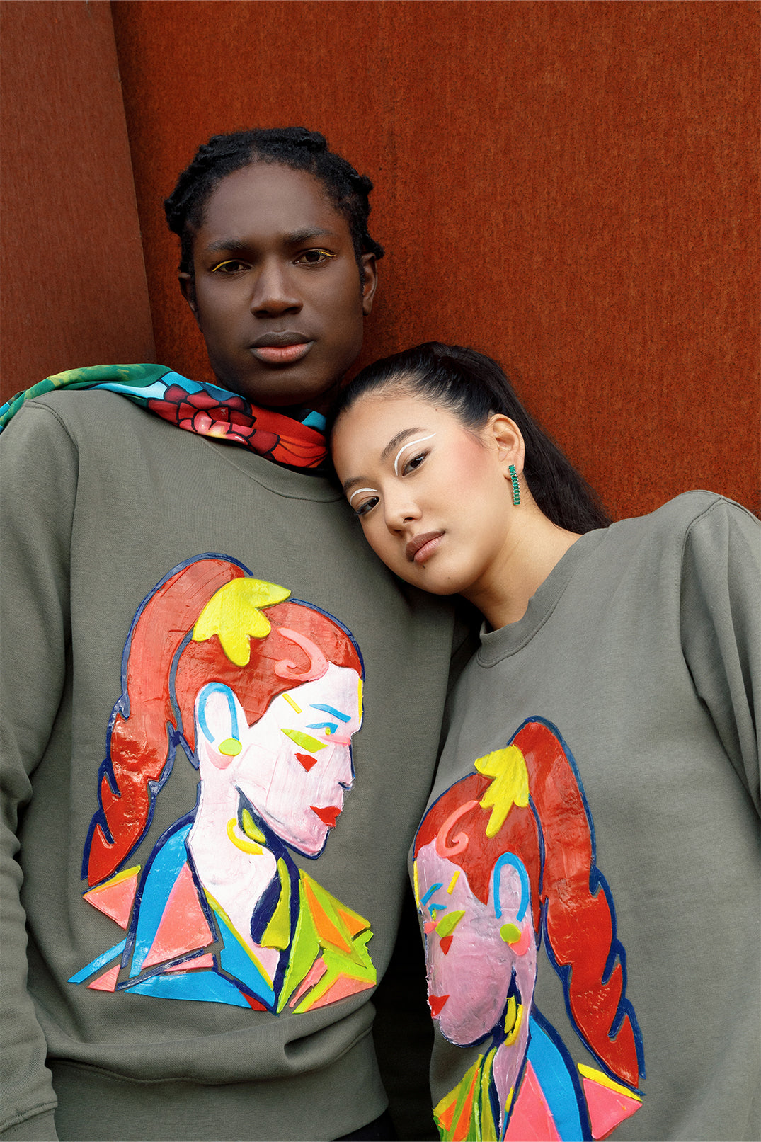 Unisex oversized green sweatshirt worn by two models, featuring a hand-crafted raised silicone abstract geometric face print, creating a three-dimensional and tactile effect.